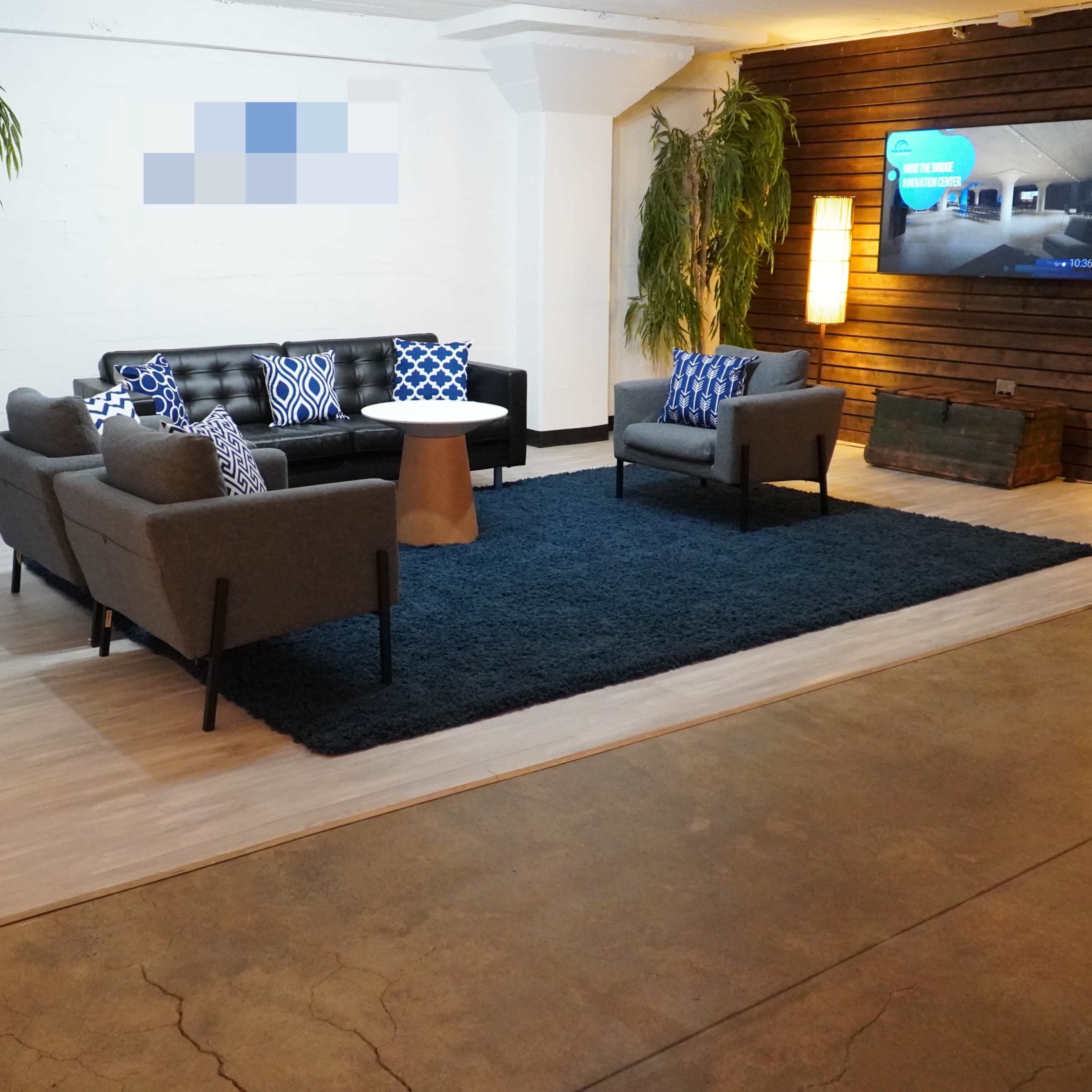A modern lounge area featuring a dark rug, a circular table, two gray sofas, and a television mounted on a wooden wall.