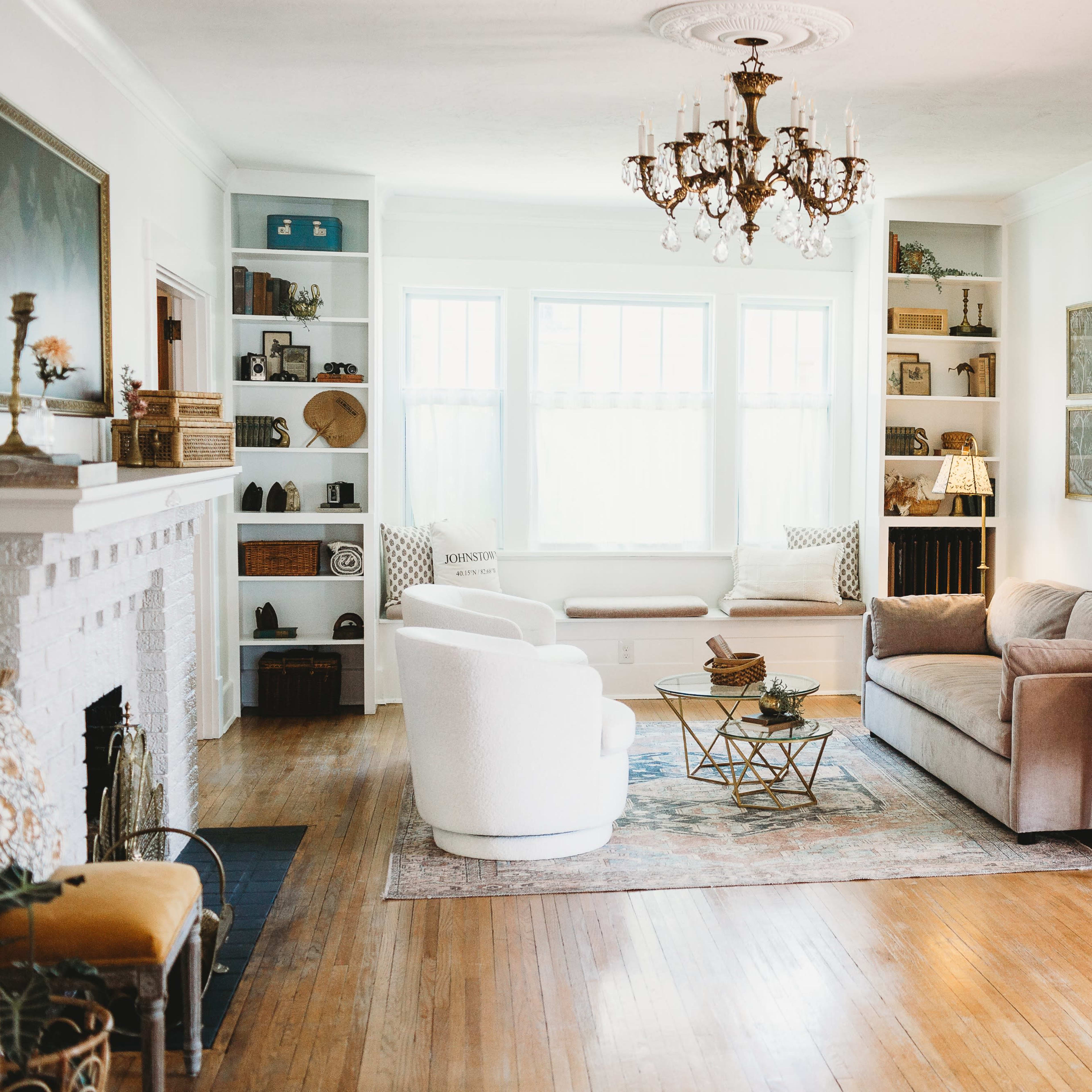 The living room features a chandelier, a white armchair, a beige sofa, a wooden coffee table, and built-in shelves filled with various decorative items.