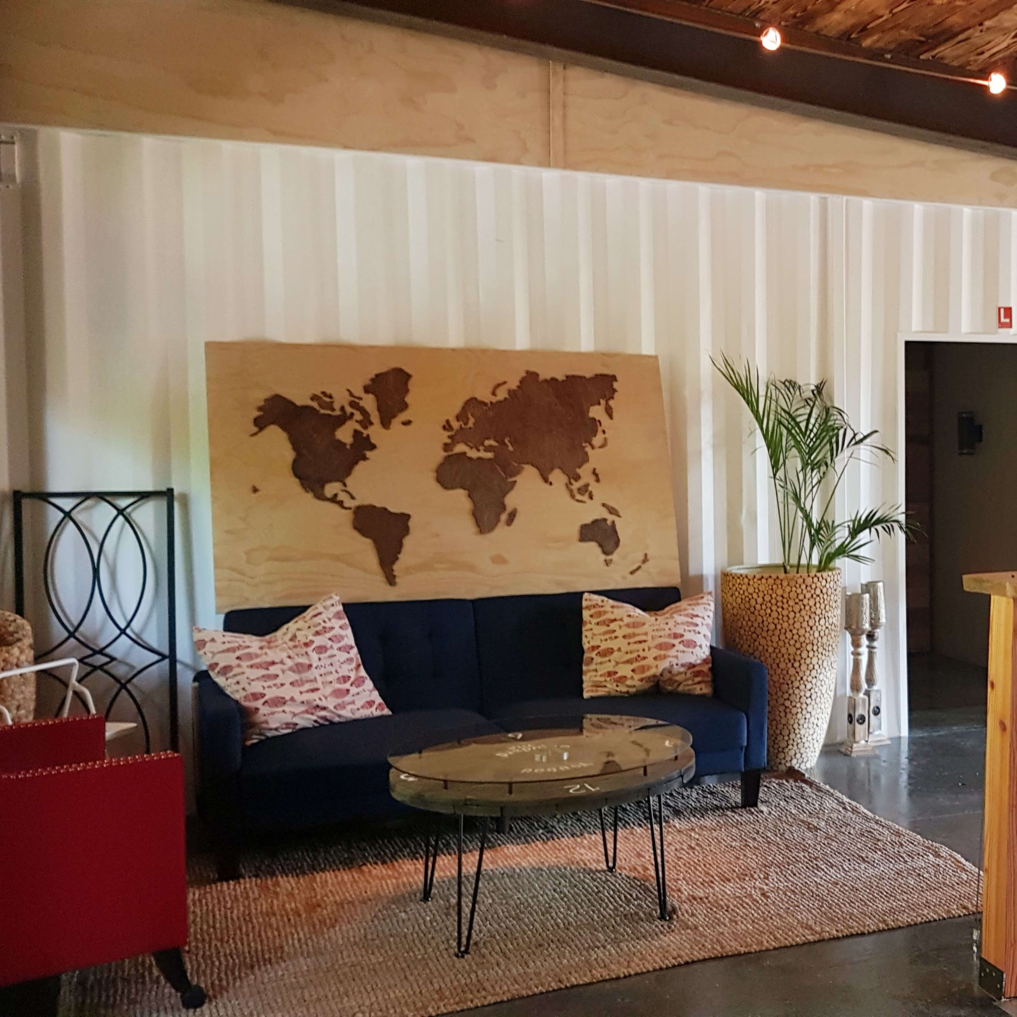 A cozy lounge area features a blue sofa, a world map on the wall, and a wooden railing overlooking a lower level.
