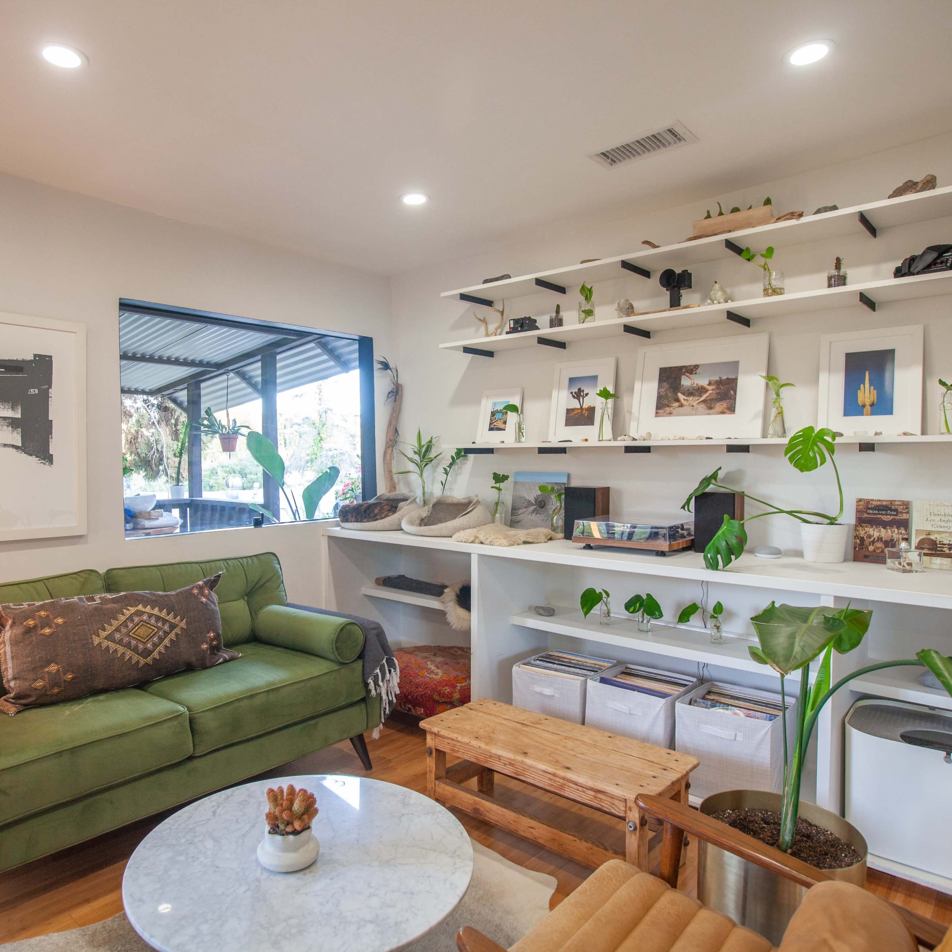 A cozy living area featuring a green sofa, a round marble coffee table, and shelves adorned with various decorative items and plants.
