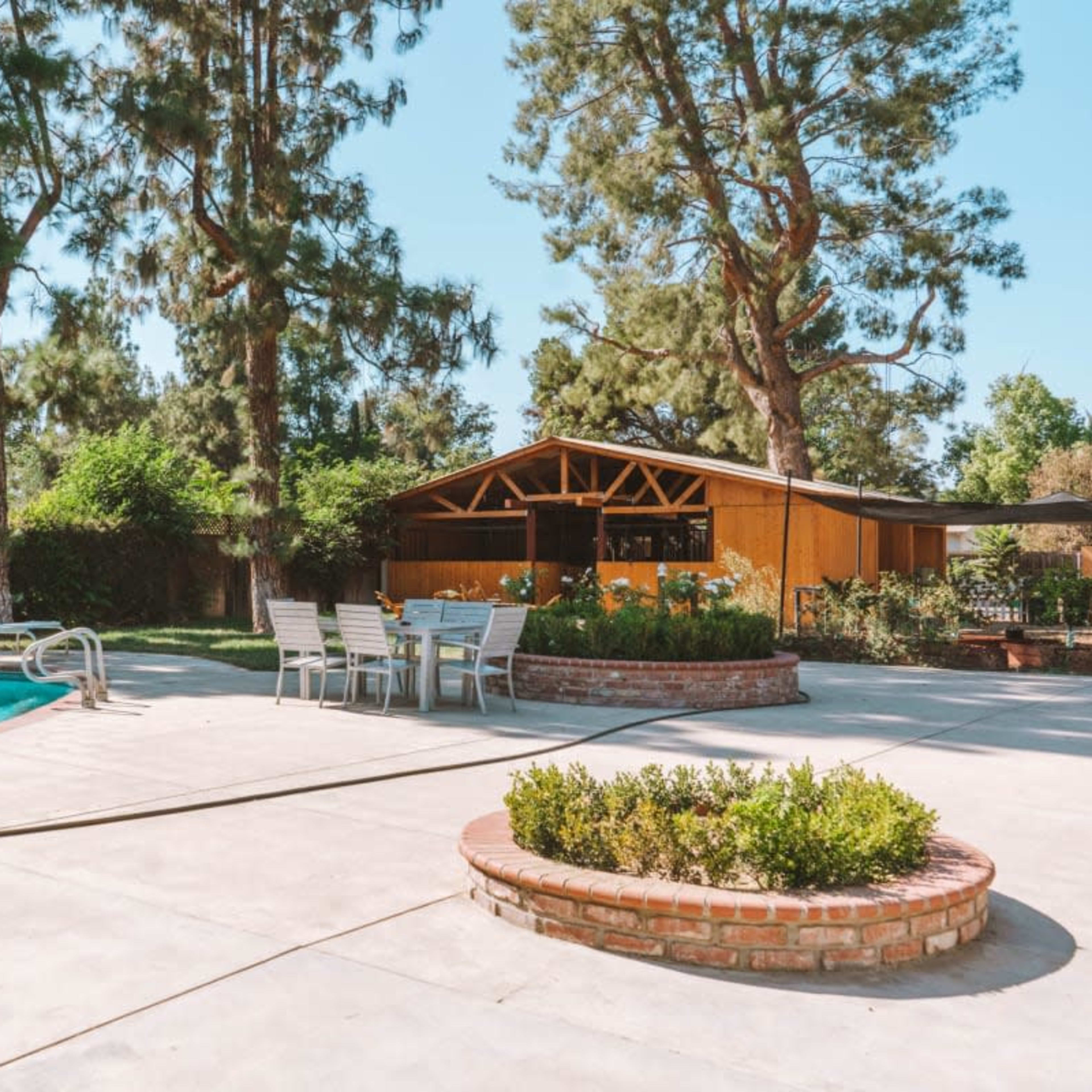 A backyard with a pool, seating area, and a wooden structure surrounded by trees and greenery.