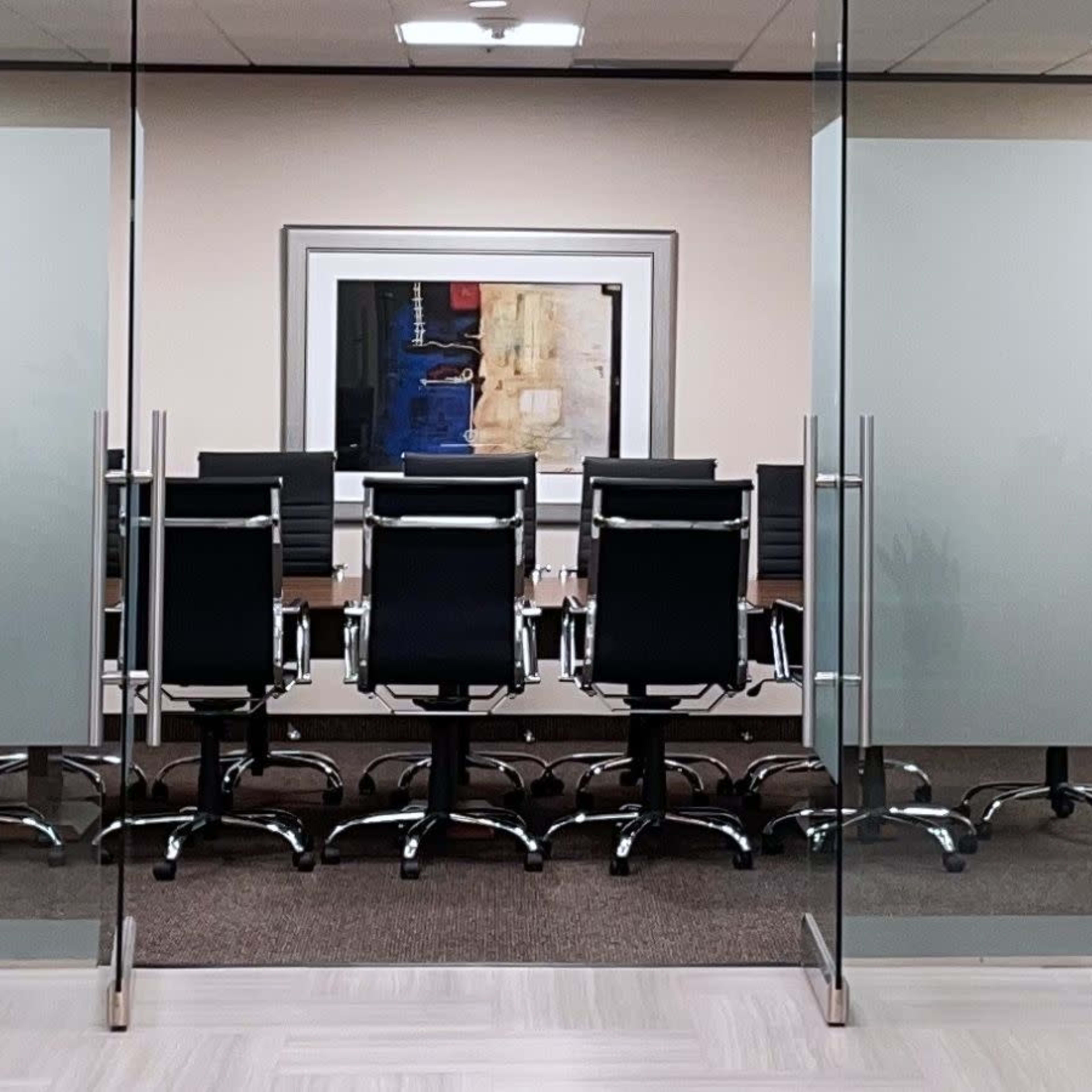 A modern conference room with a long table and black rolling chairs is visible through glass doors.
