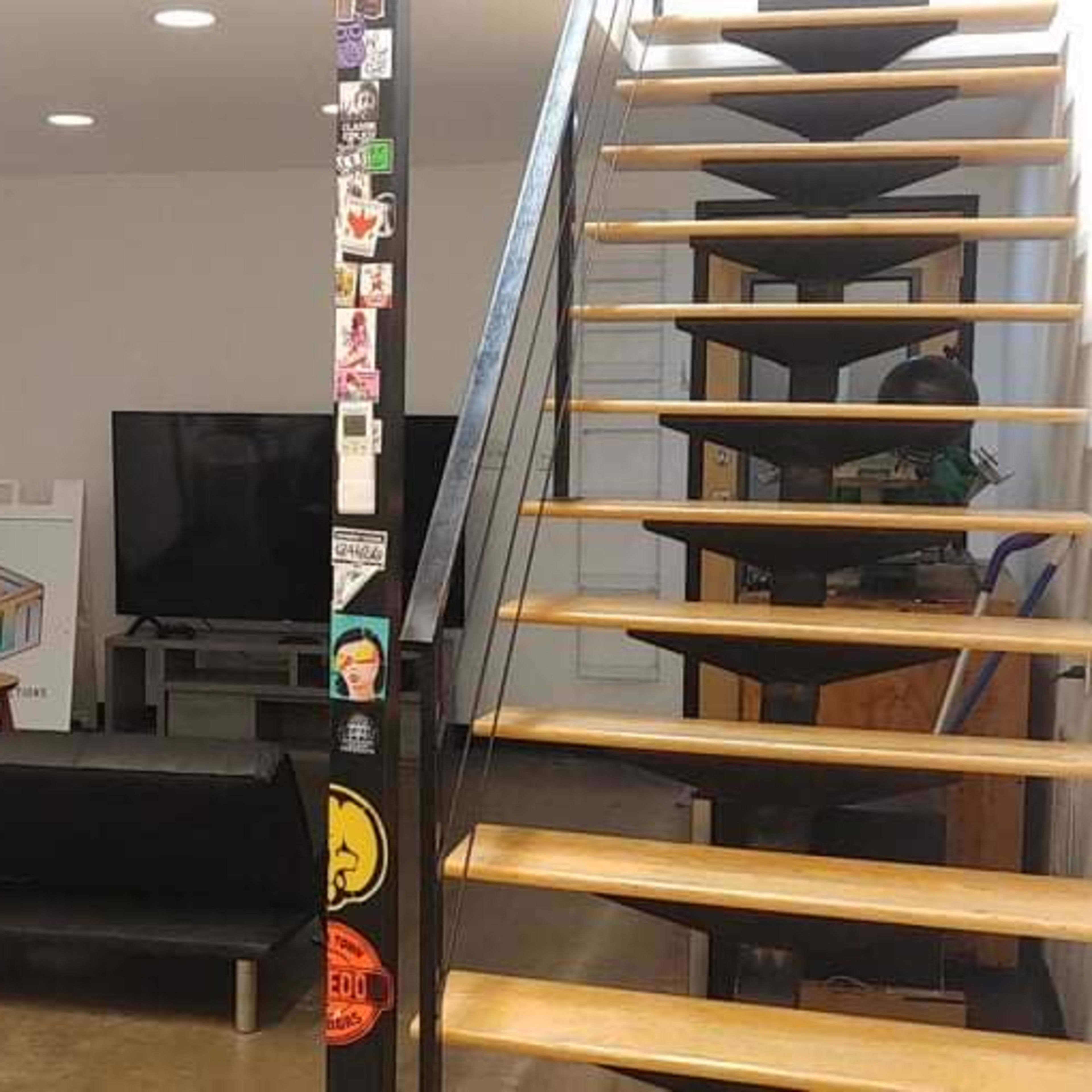 A modern living room on the left with a black couch and a television, and a stairway on the right leading to an upper level.