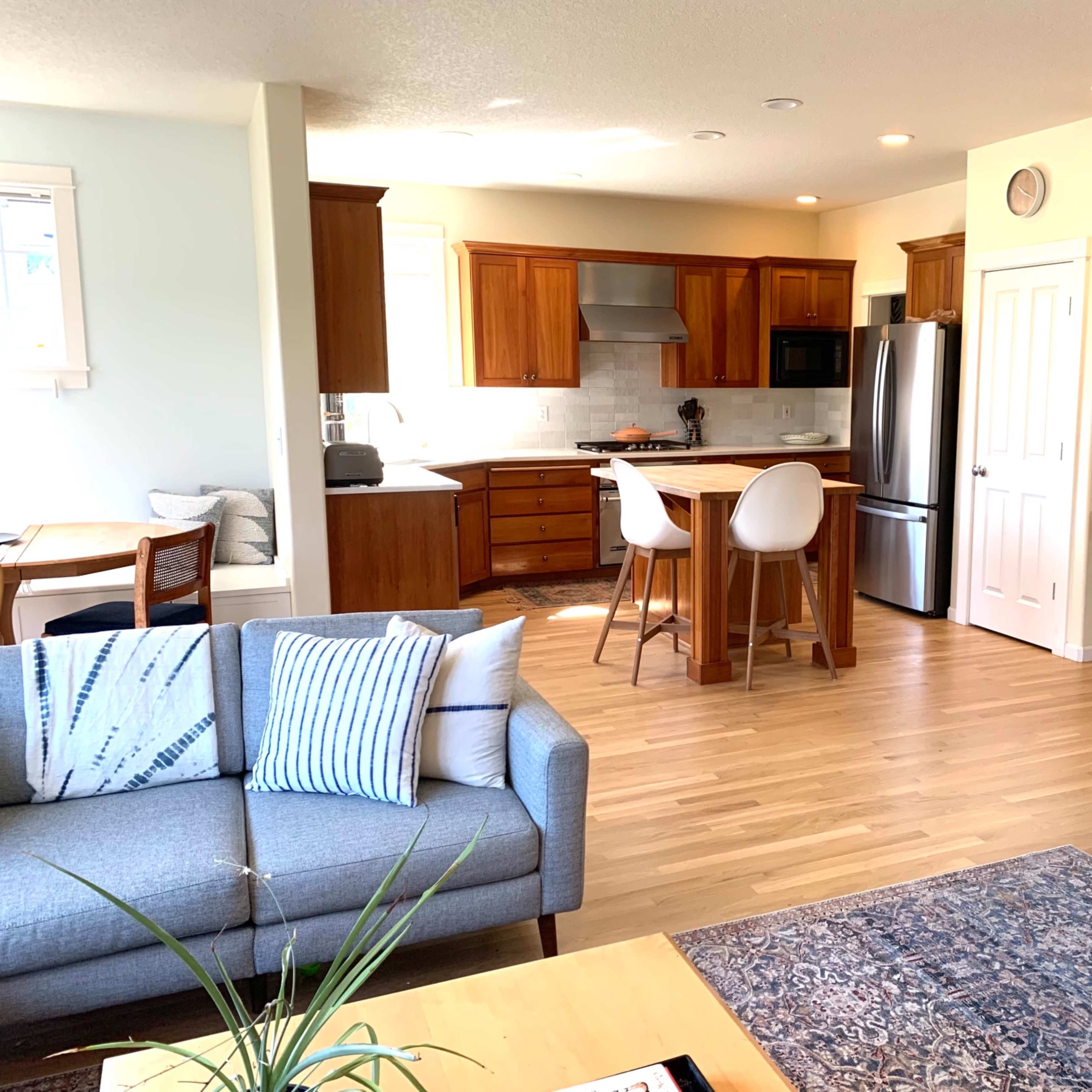 A modern open-concept kitchen and living area with wooden cabinets, stainless steel appliances, and a comfortable seating arrangement.