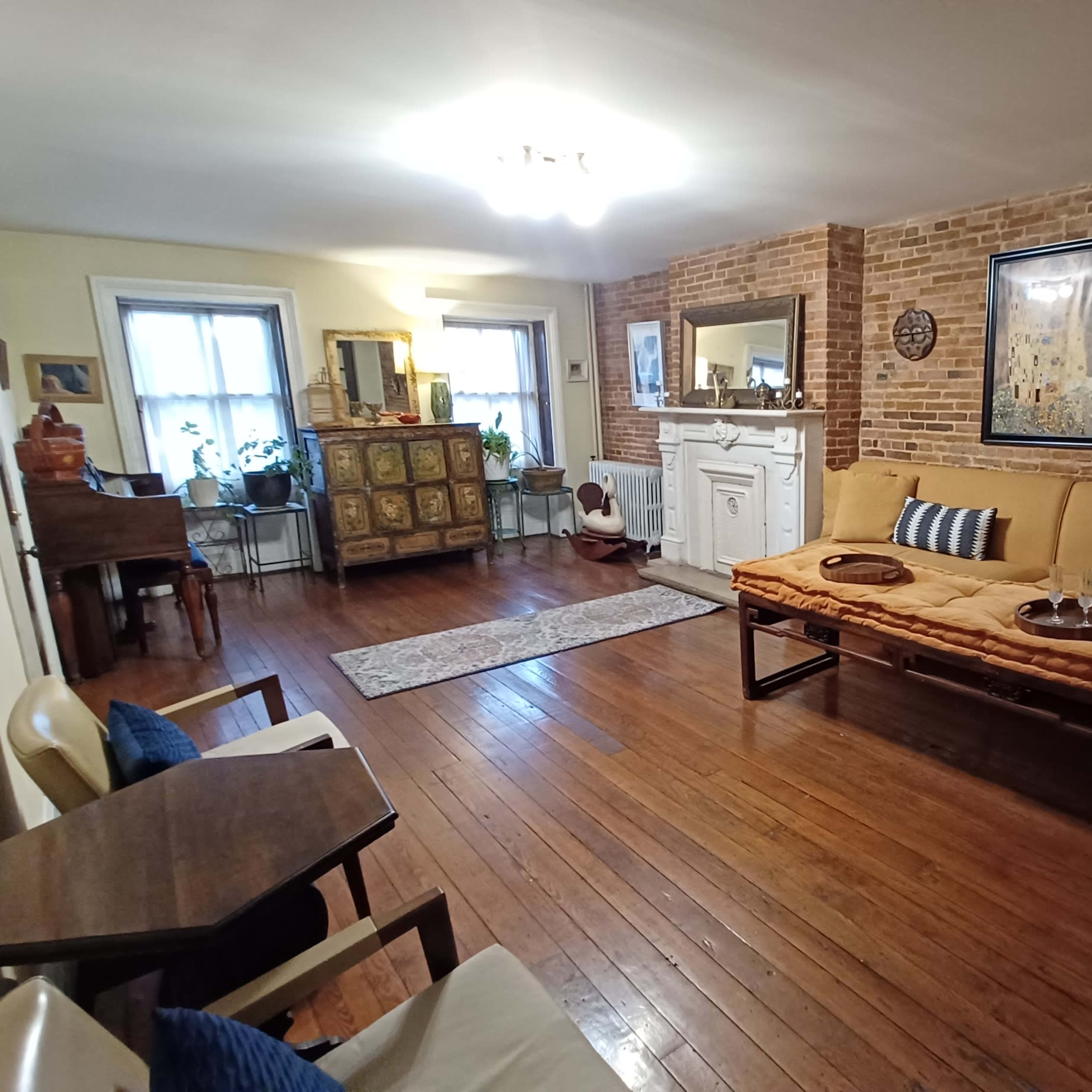 A living room with exposed brick walls, hardwood floors, a sofa with cushions, and decorative elements including artwork and a small piano in the background.