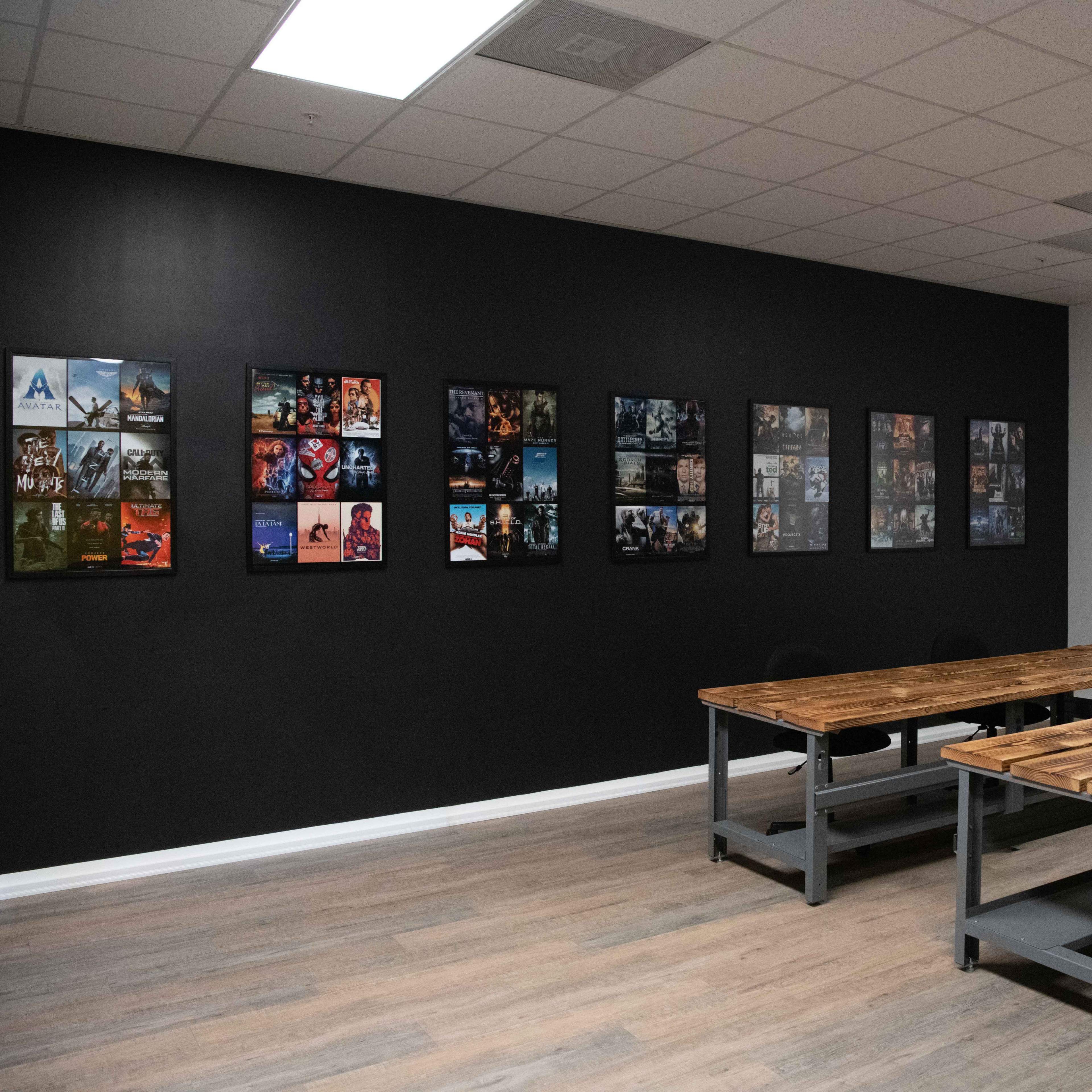 A meeting room features a wooden table surrounded by chairs, with a gallery of framed images displayed on the black wall.