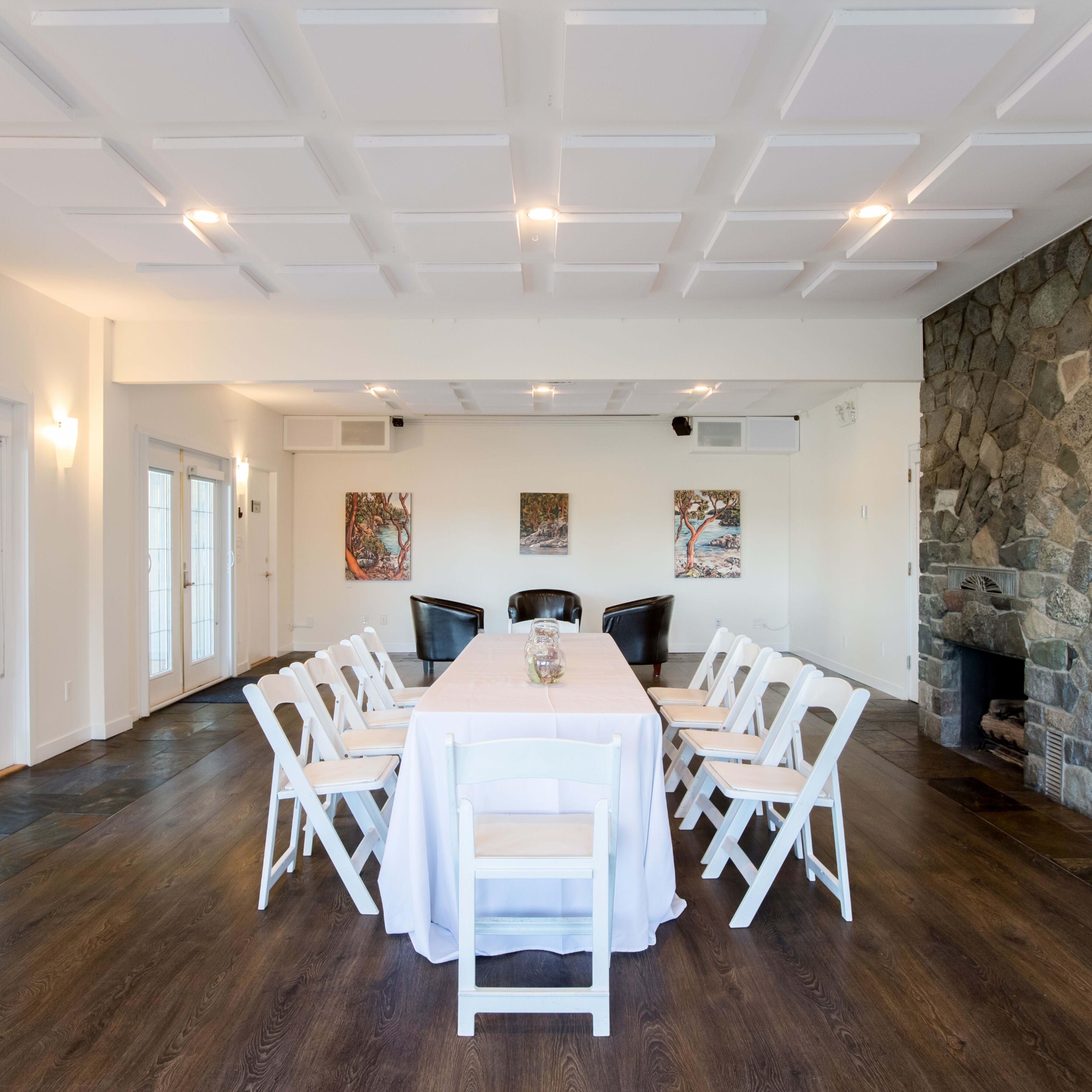 A conference room features a long table with white chairs, stone walls, and artwork on display.