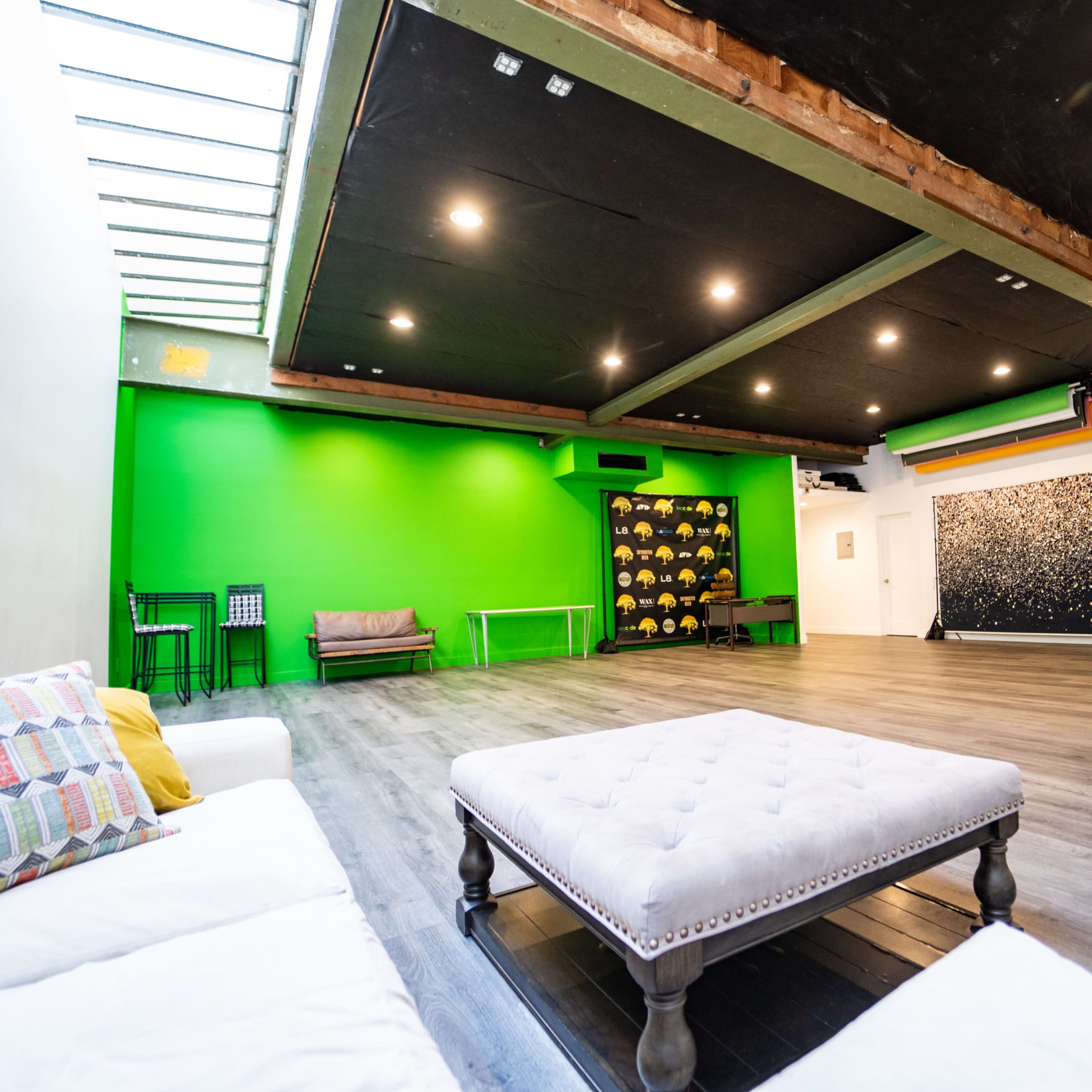 A spacious room featuring a green wall, a tufted coffee table in the center, and a seating area with a couch and chairs along one side.
