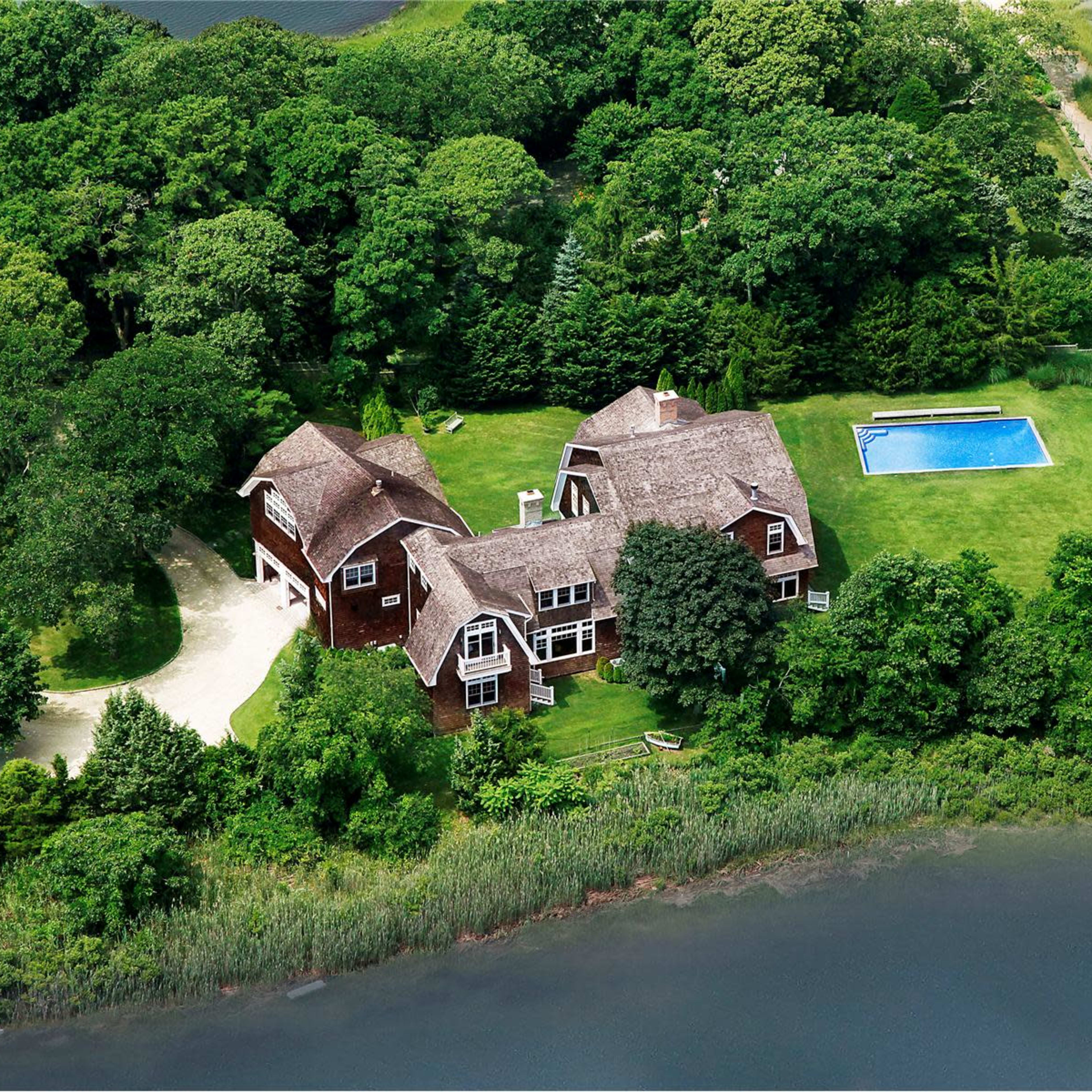A large home surrounded by greenery, with a swimming pool in the yard and water nearby.