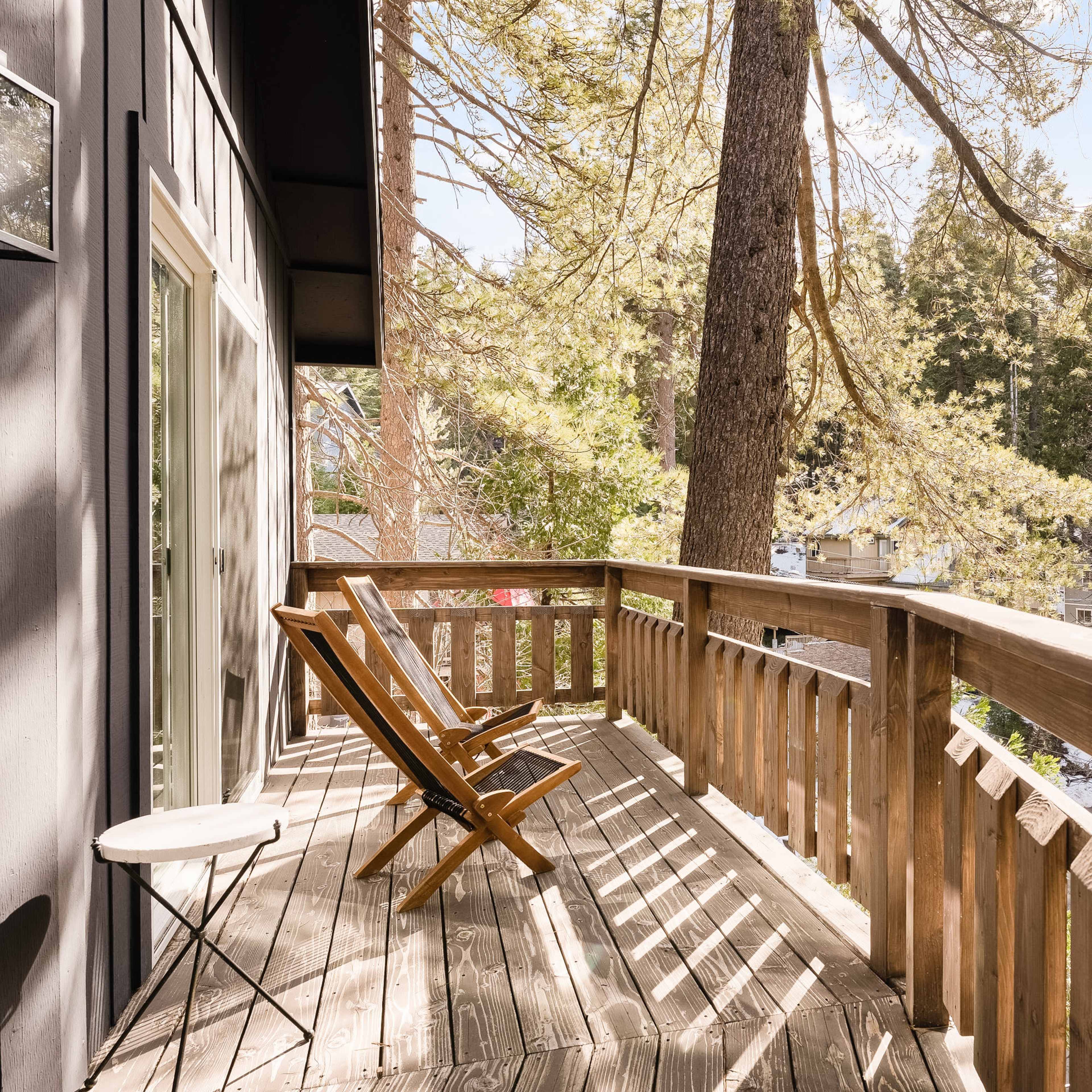 A wooden deck with two folding chairs overlooking a forest of tall trees.