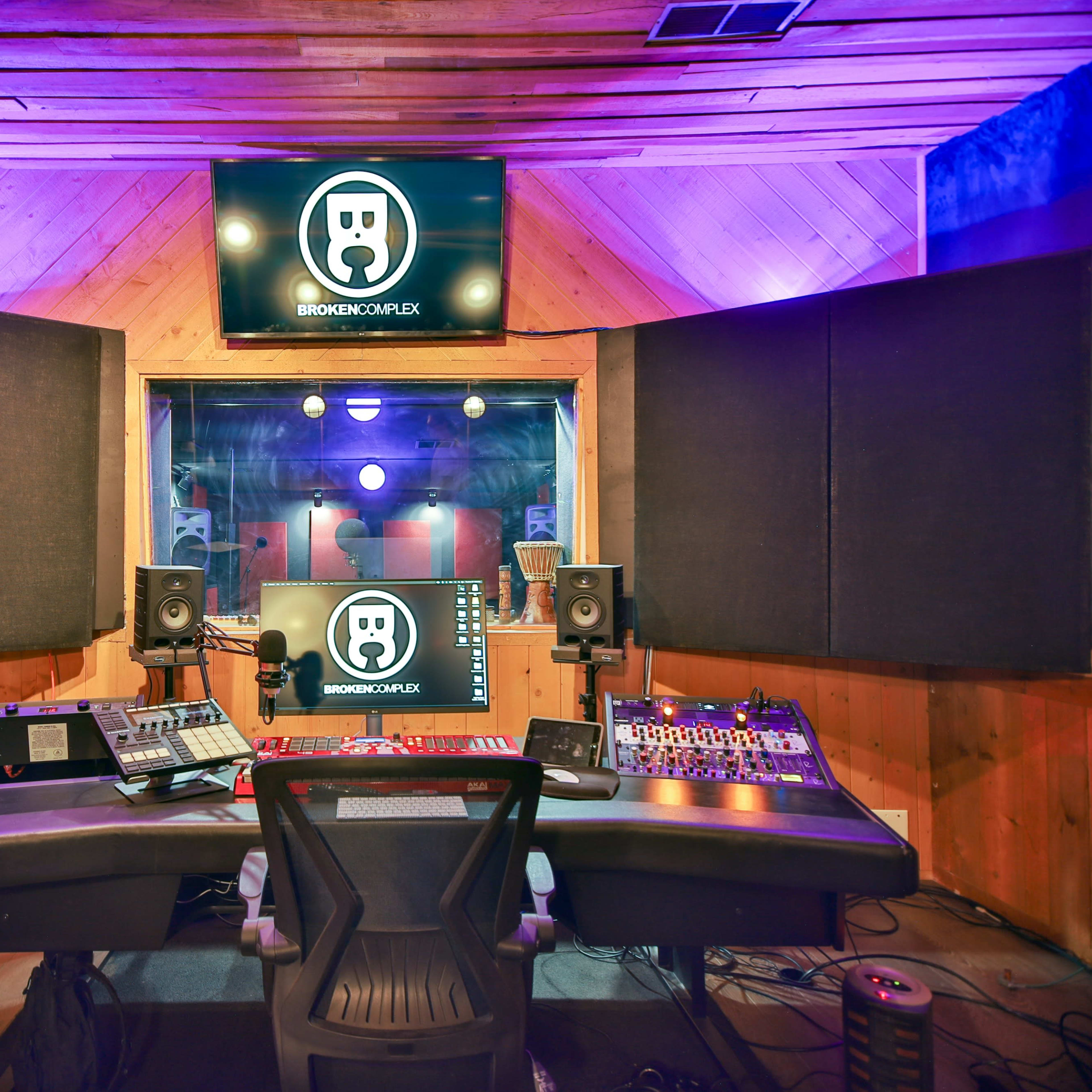 A music production studio featuring a control desk, speakers, and a large screen displaying a logo.