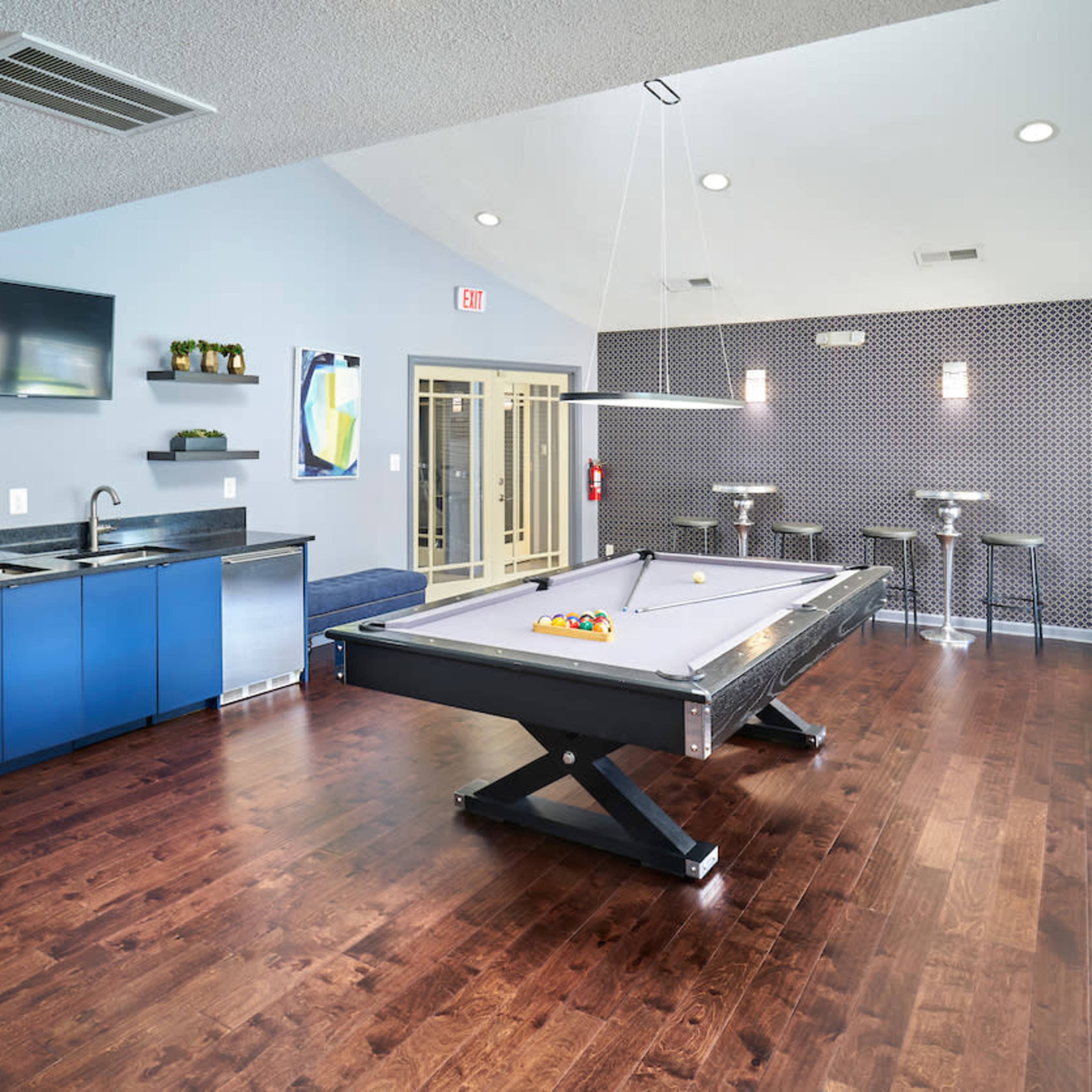 A modern lounge area featuring a pool table, a kitchenette, and seating along the walls.