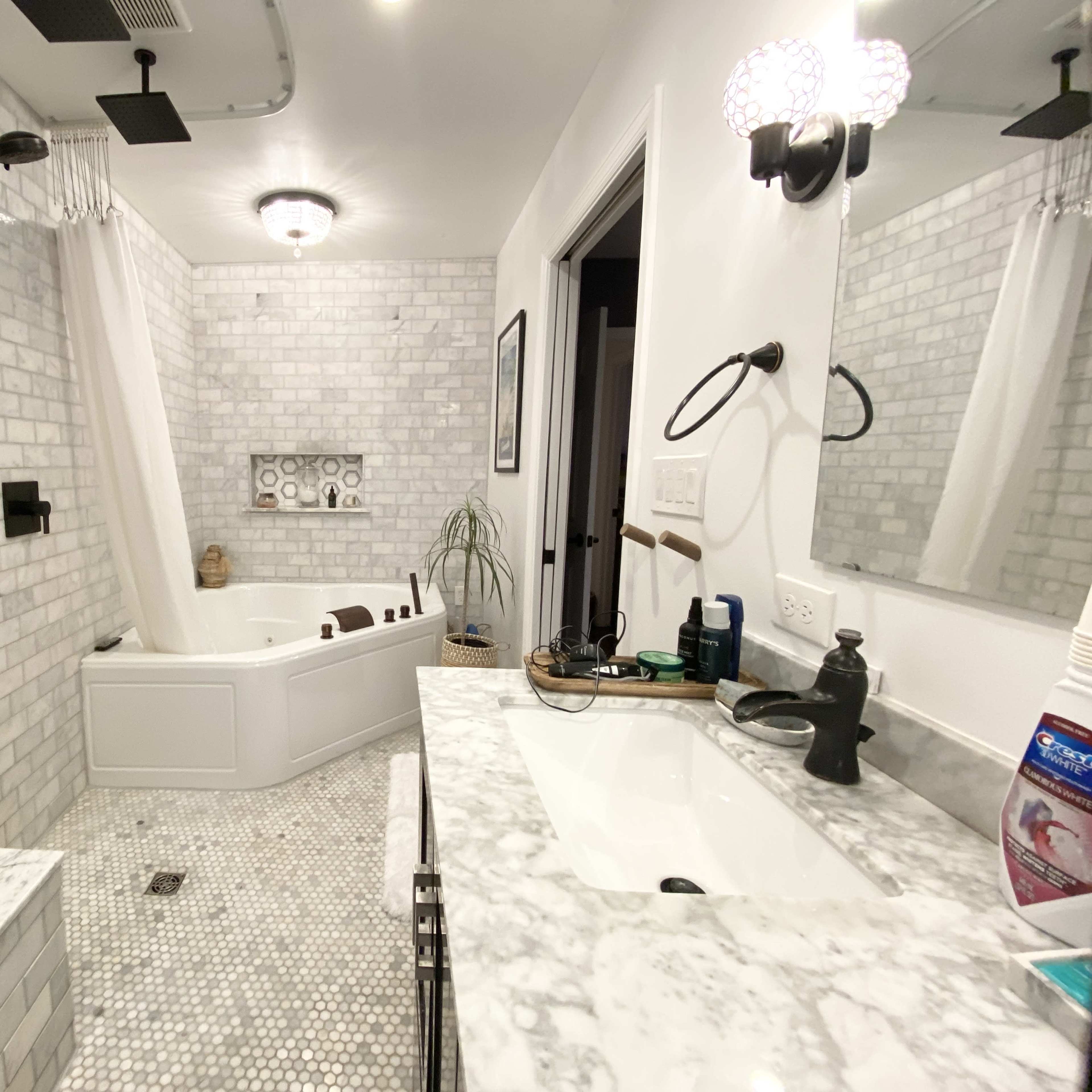 A modern bathroom featuring a marble countertop, a freestanding bathtub, a walk-in shower with black fixtures, and a tiled wall.