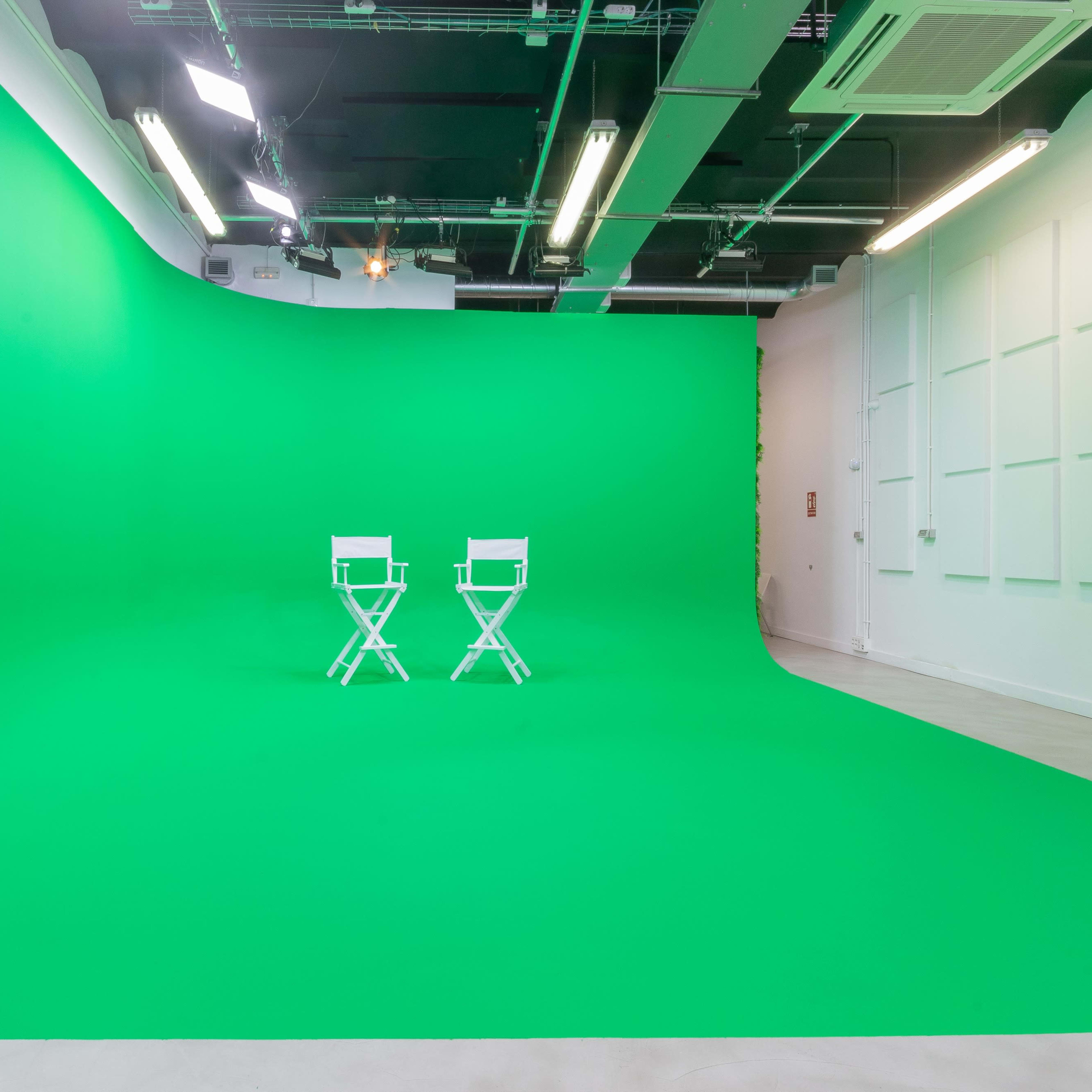 A photography studio featuring a curved green backdrop and two white director's chairs positioned in front.