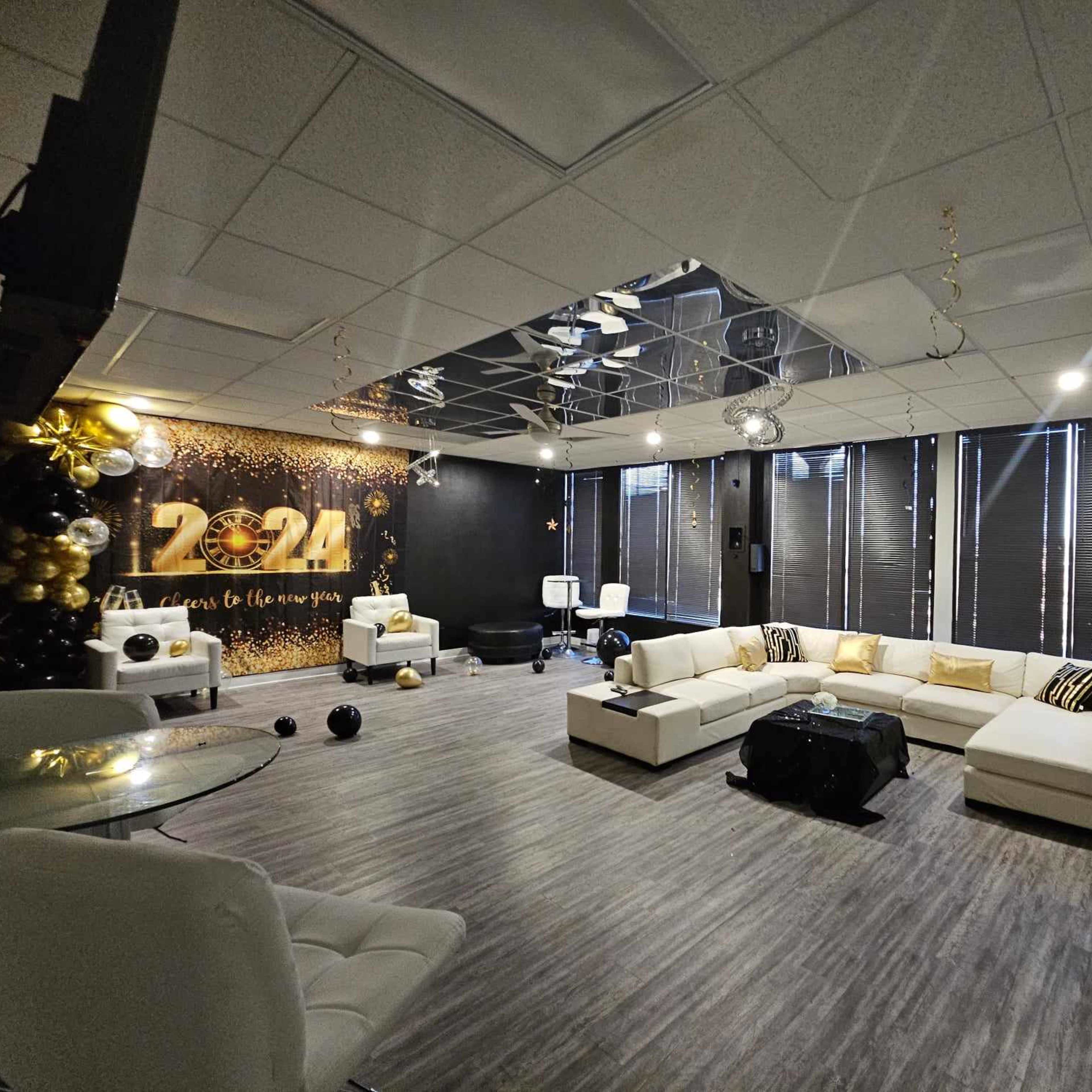 A modern event space decorated with black and gold balloons, featuring a white seating area and a wall adorned with "2024" in large numerals.