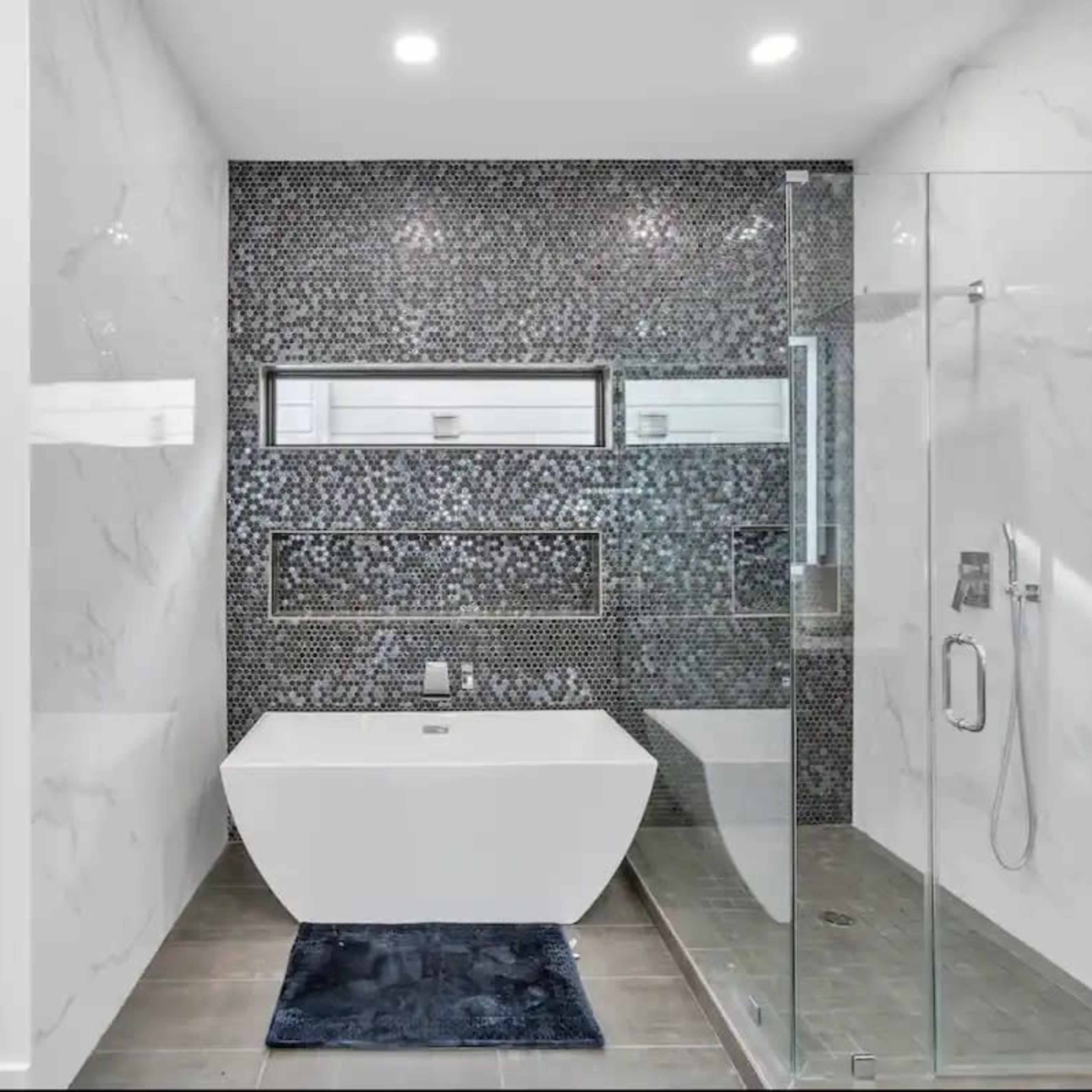 A modern bathroom featuring a freestanding bathtub, a glass shower enclosure, and a wall adorned with mosaic tiles.