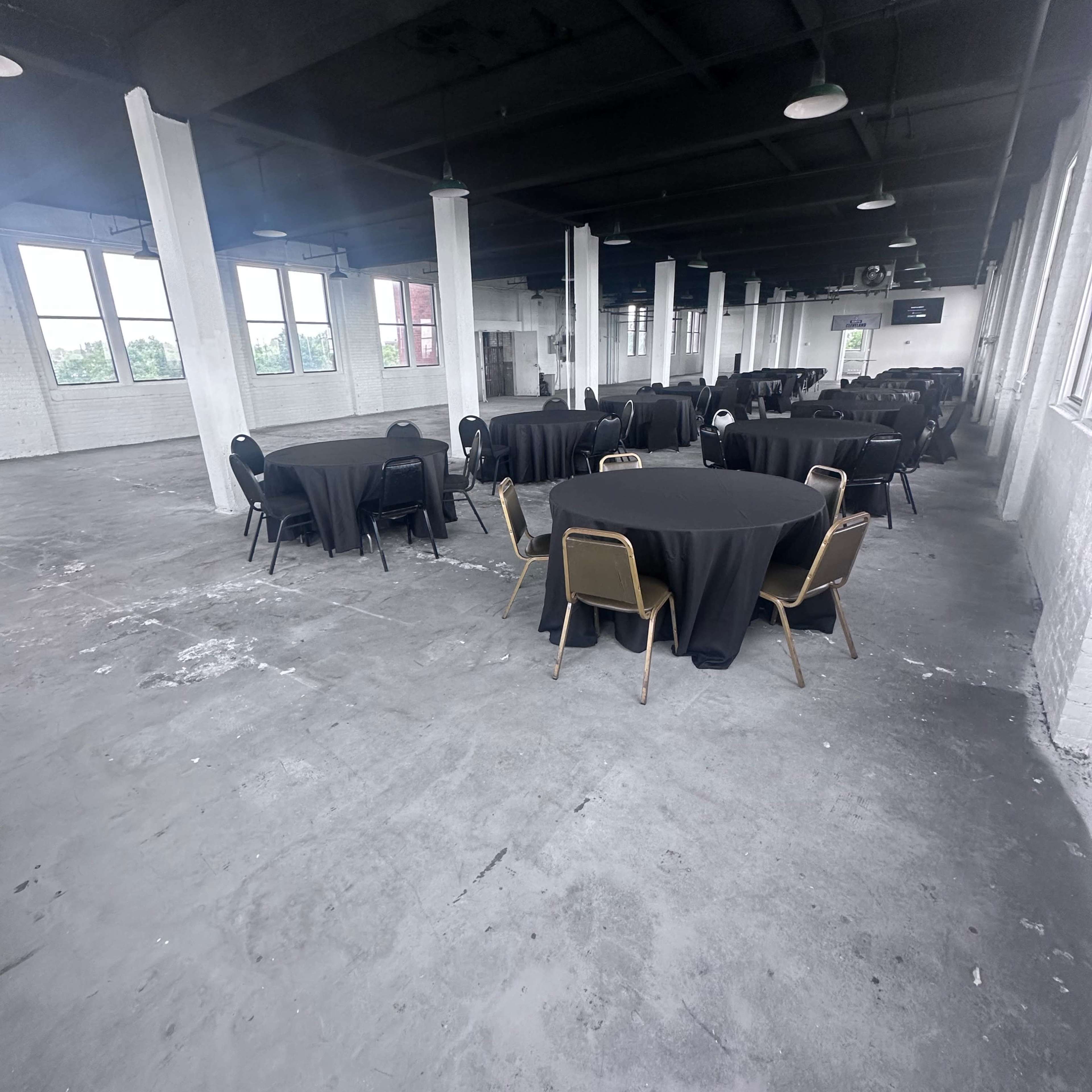 A large, vacant room set up with multiple round tables covered in black tablecloths.