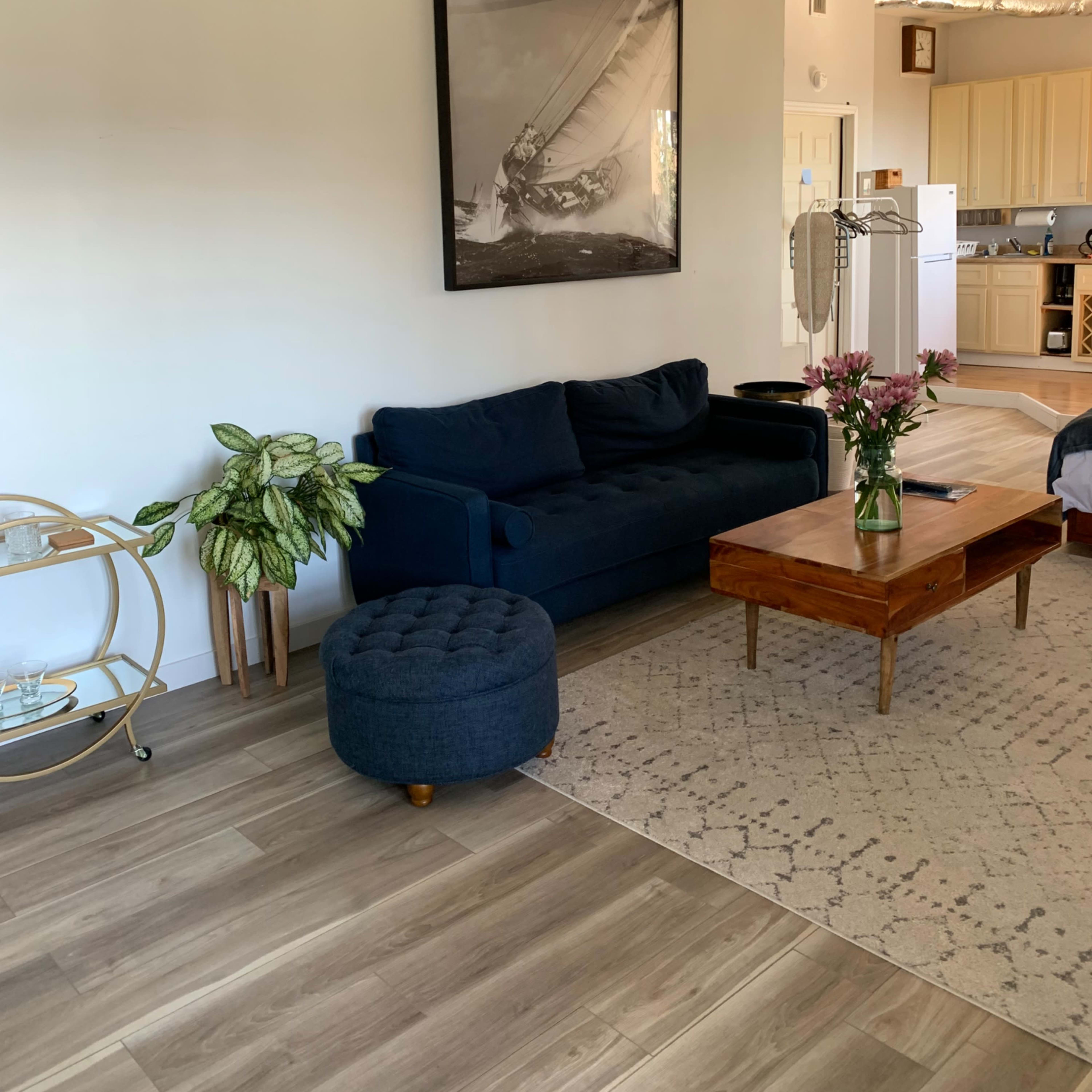 A living room with a navy blue sofa, a wooden coffee table, a decorative cart, and a kitchen area visible in the background.
