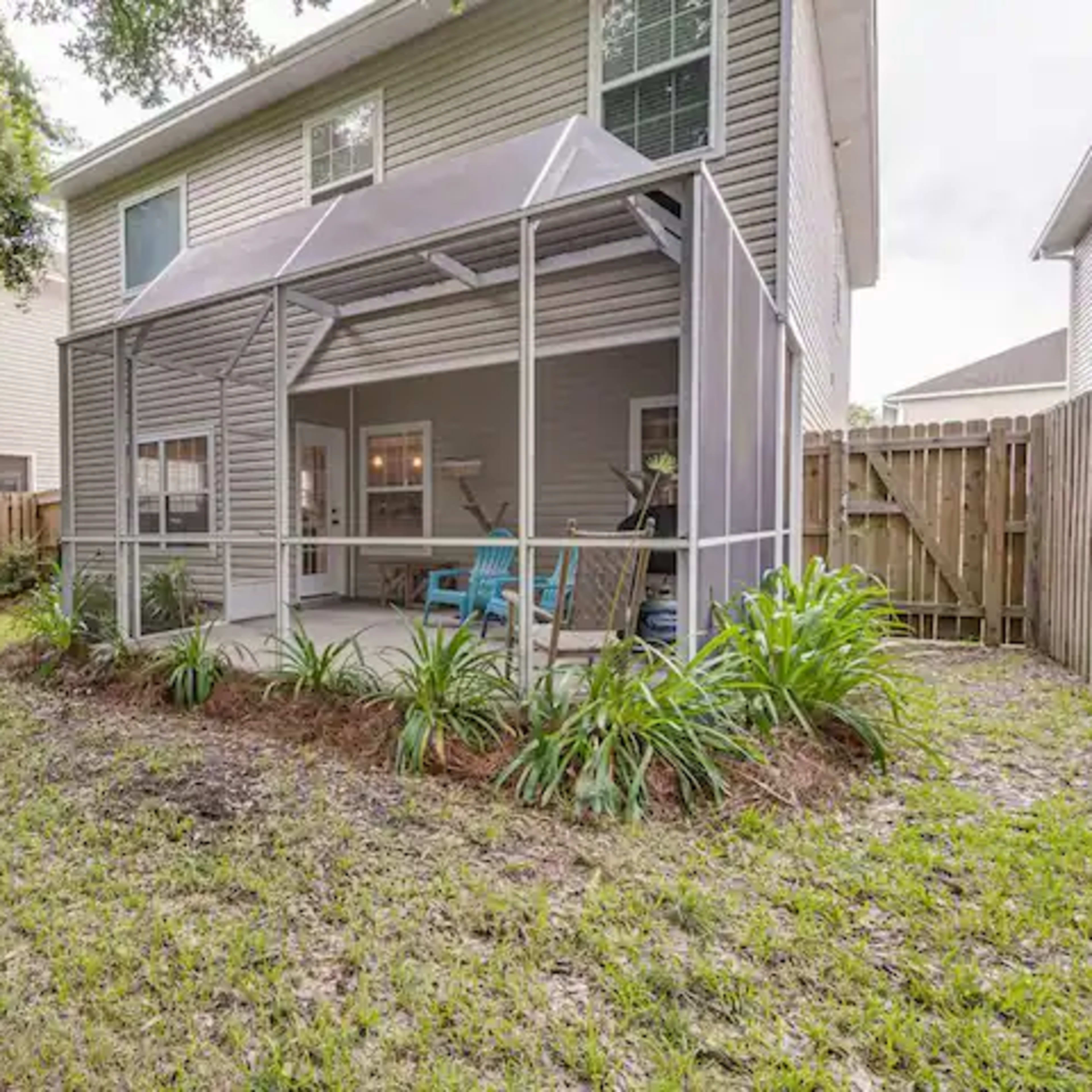A backyard with a screened porch and a lawn area surrounded by a wooden fence.