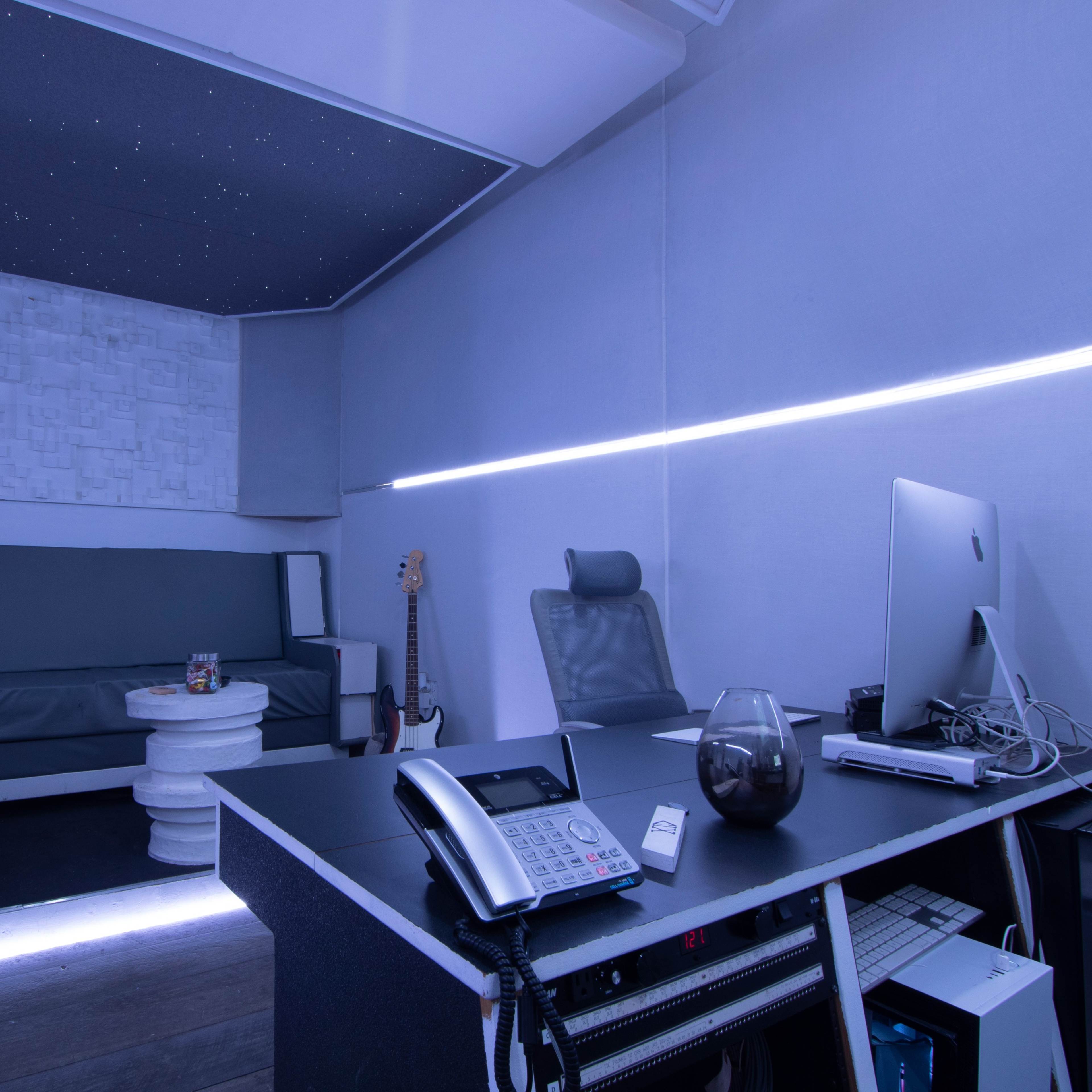 A modern office space featuring a desk with a computer, a telephone, and a round white table surrounded by a couch and a guitar.