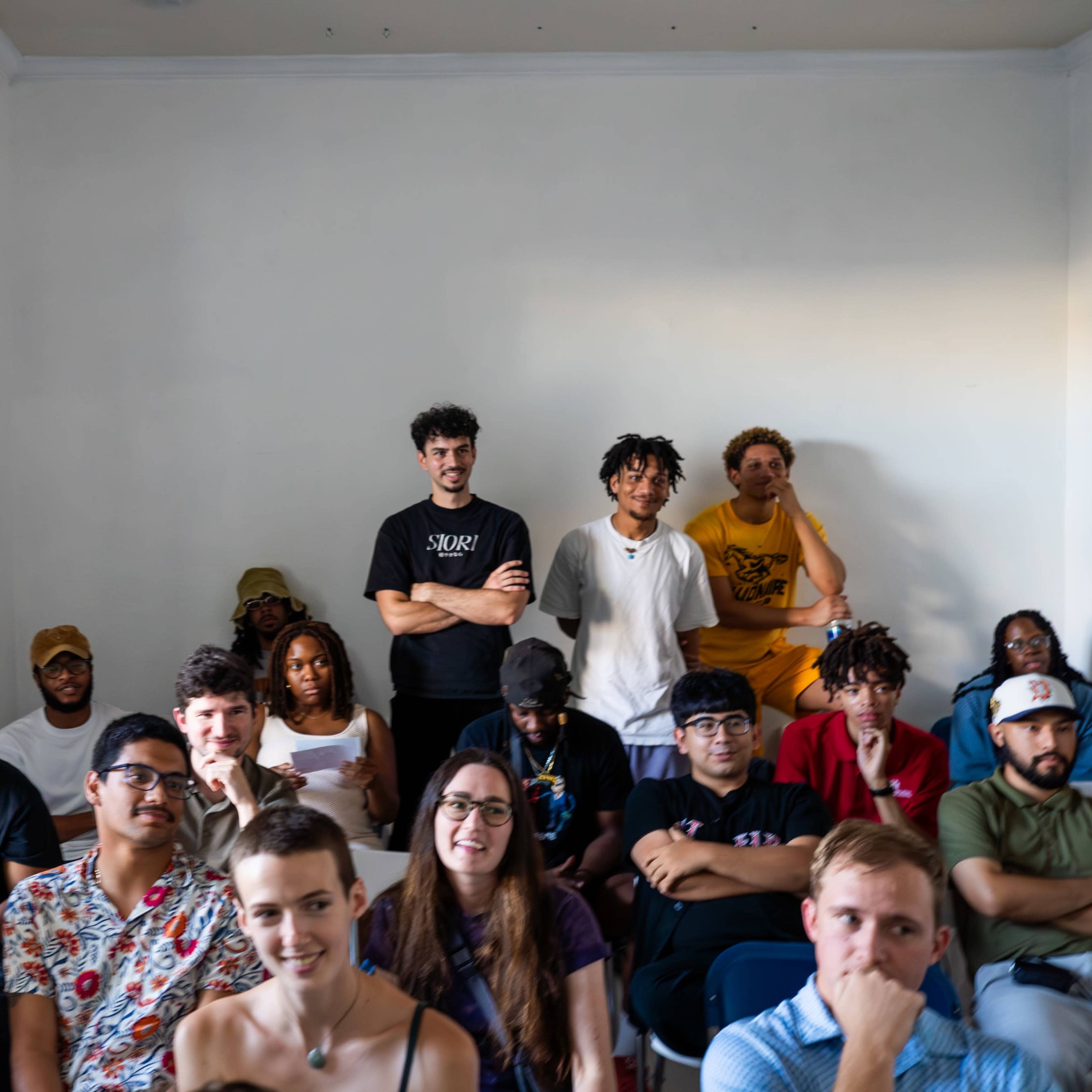 A diverse group of people is seated in rows, facing forward in a brightly lit room.