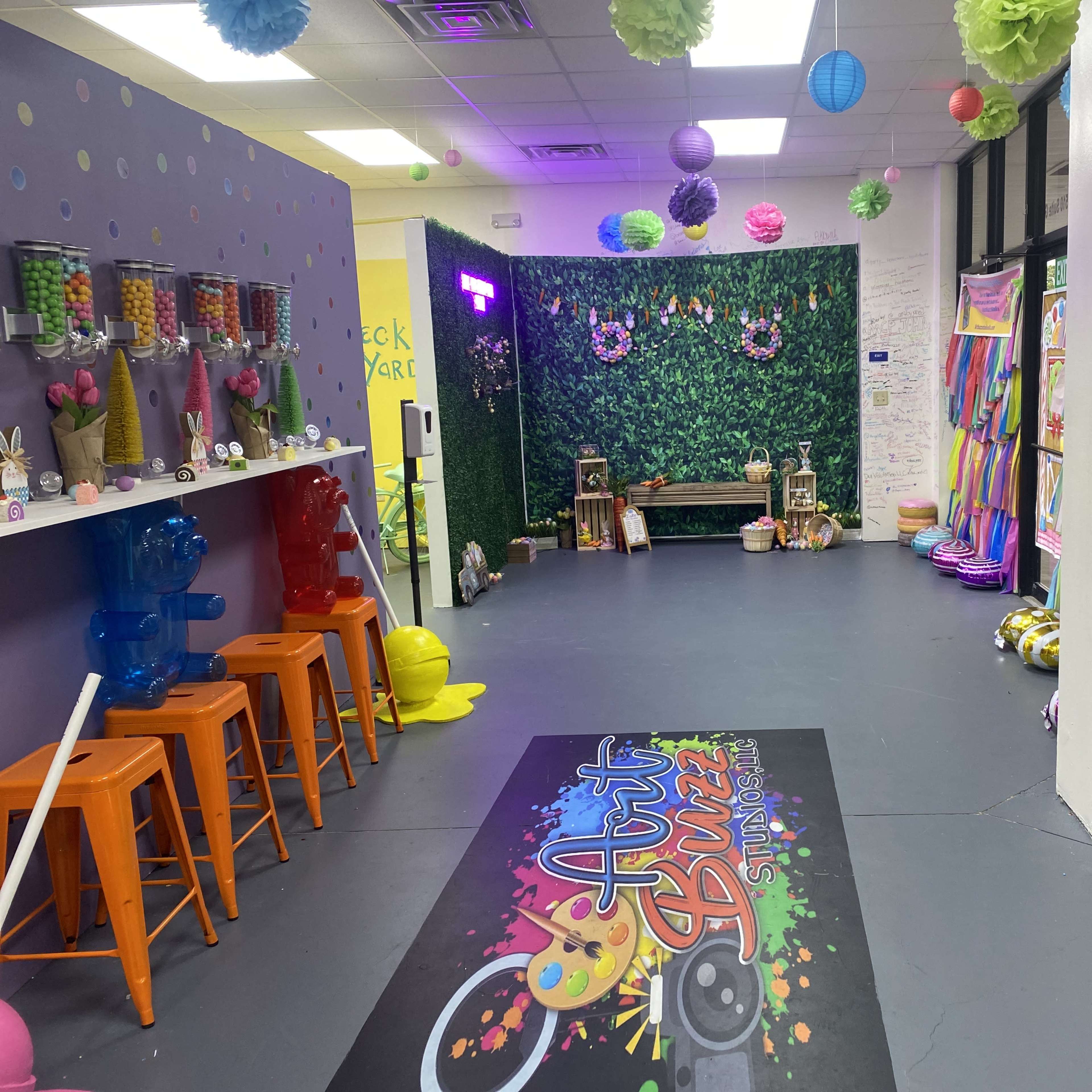 A colorful recreational space featuring a vibrant activity area, a snack bar with orange stools, and a backdrop of greenery along with various decorations.