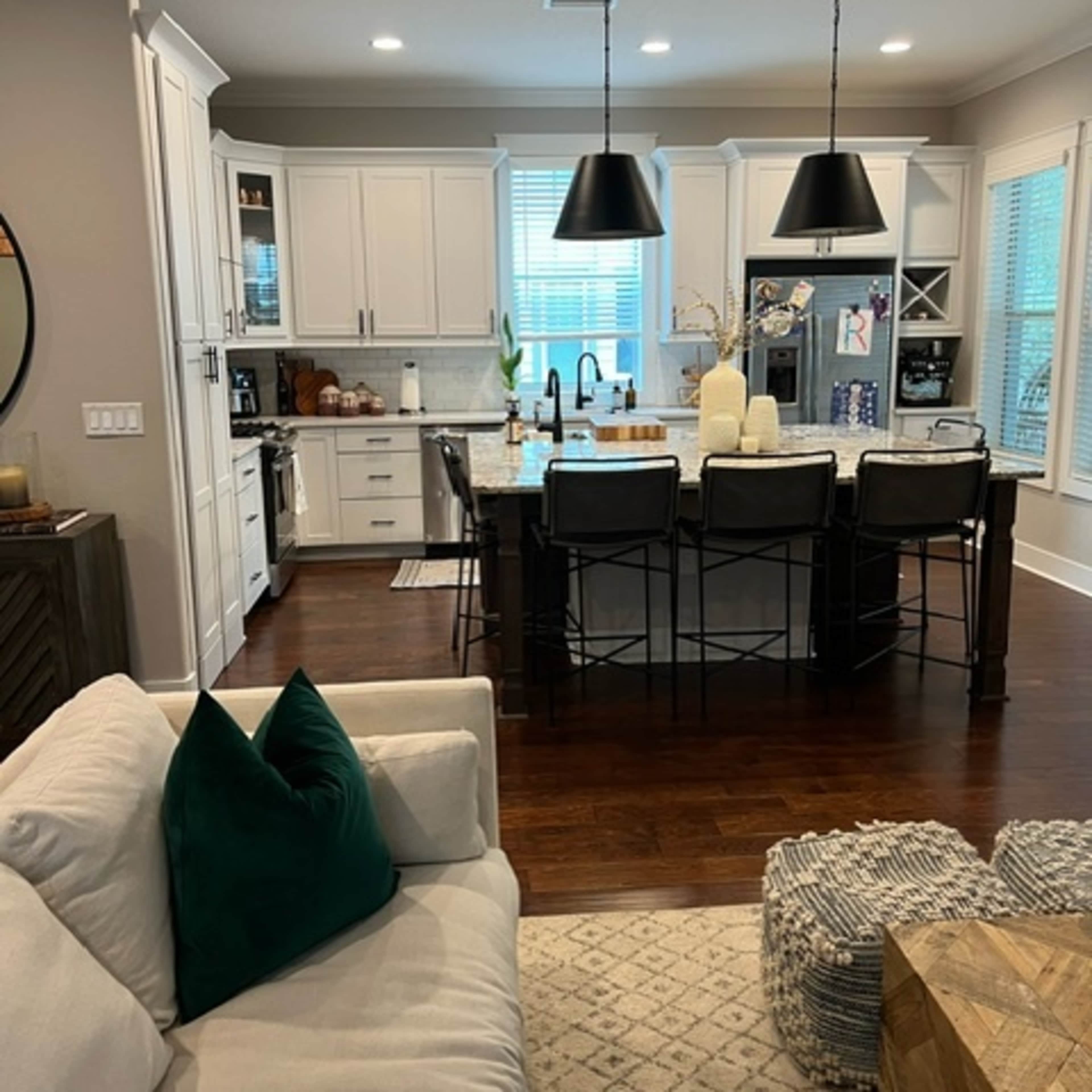 A modern kitchen features white cabinetry, dark pendant lights, and a large island with bar seating.