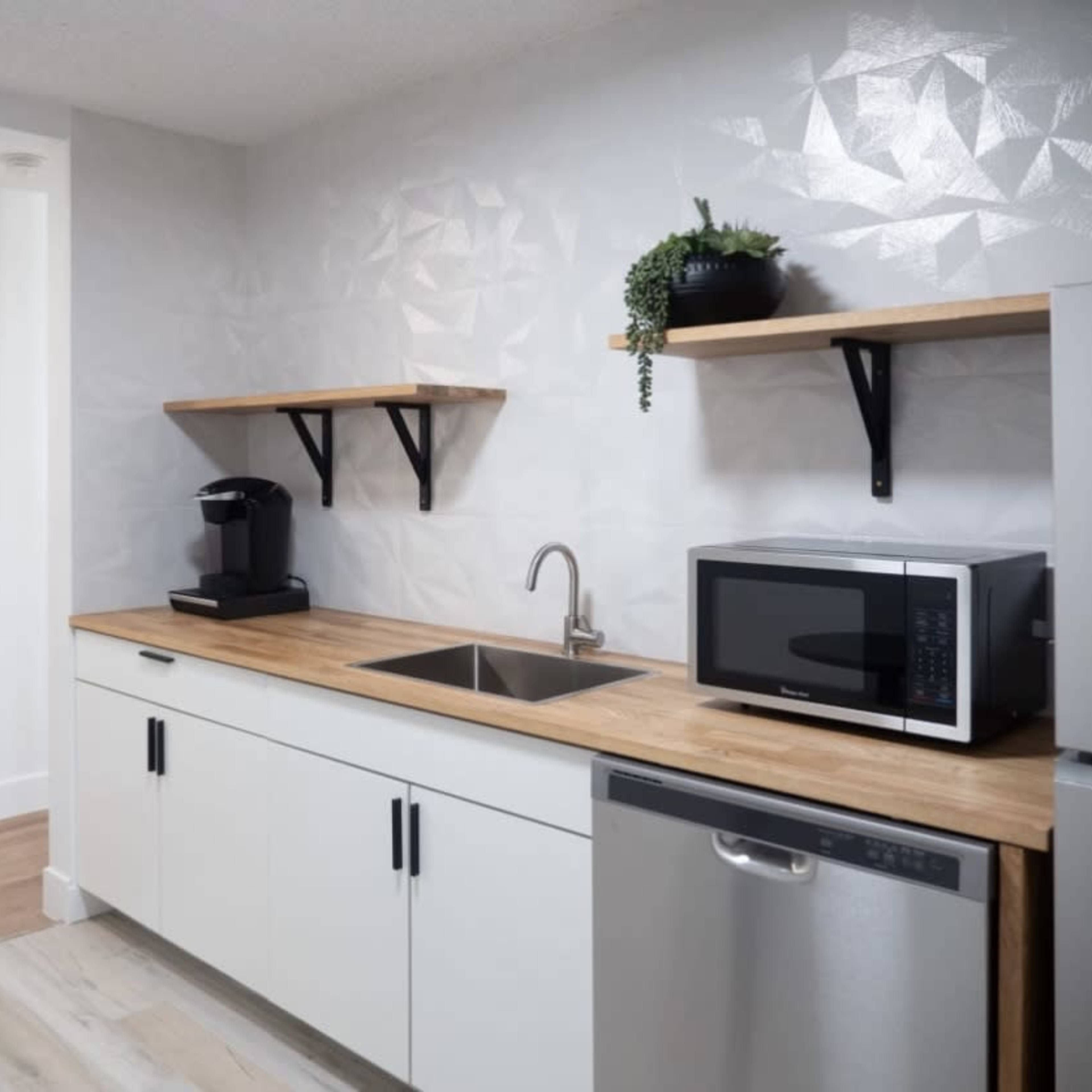 A modern kitchen with a wooden countertop, a sink, a microwave, a coffee machine, and open shelves for storage.