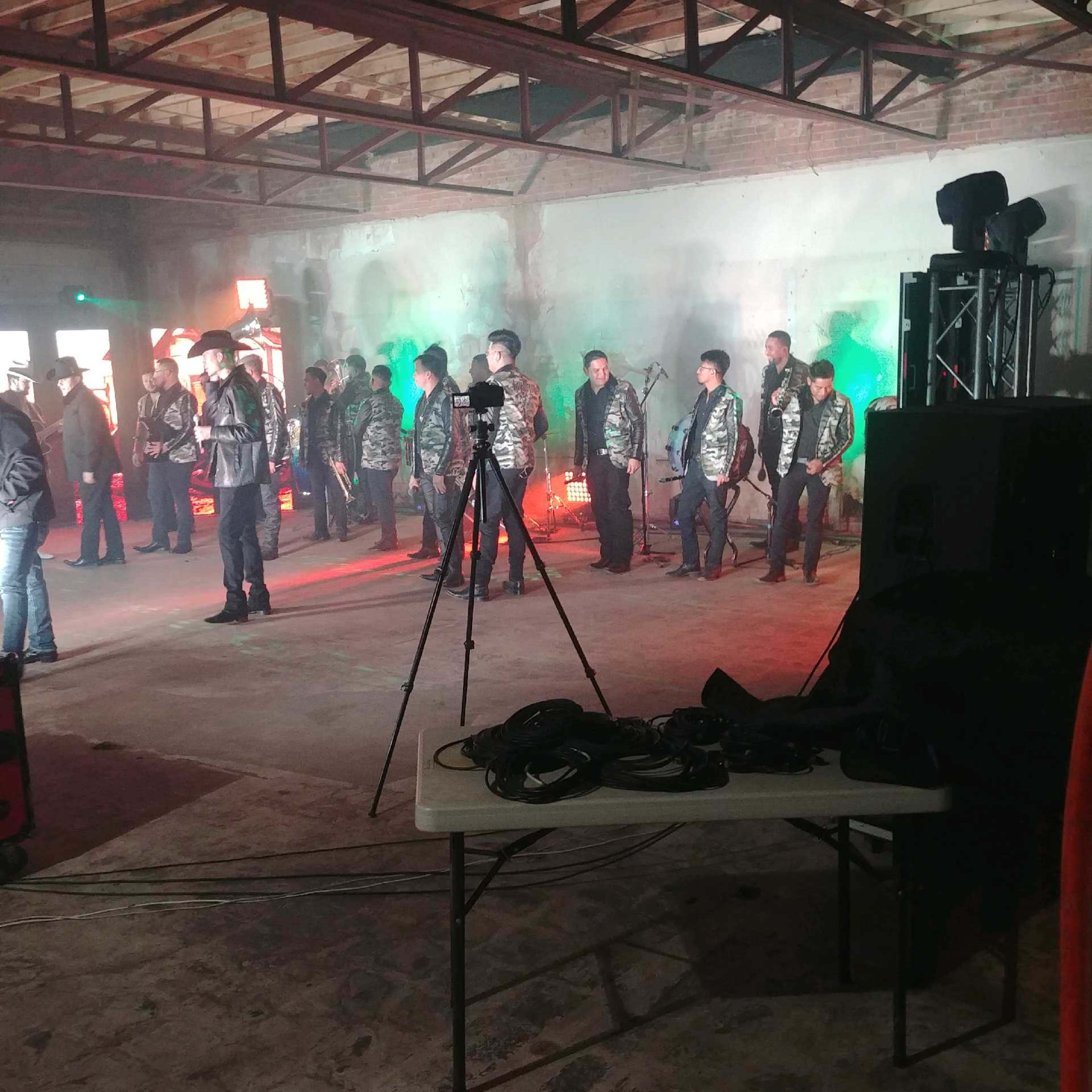 A group of people in jackets stands in a dimly lit industrial space with green and red lighting and equipment set up for a performance or event.