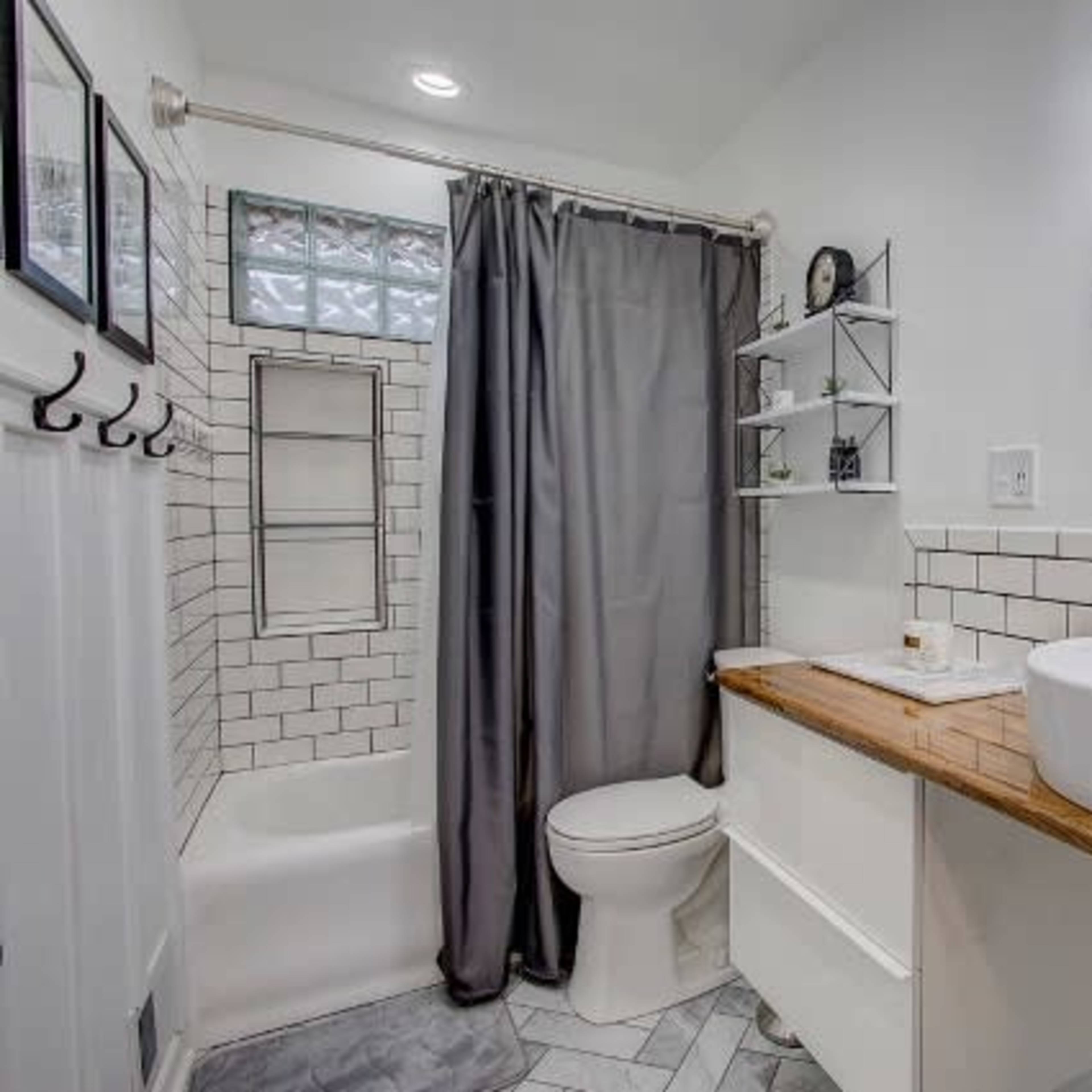 A modern bathroom featuring a shower-tub combo, a round mirror, a wooden sink countertop, and gray curtains.