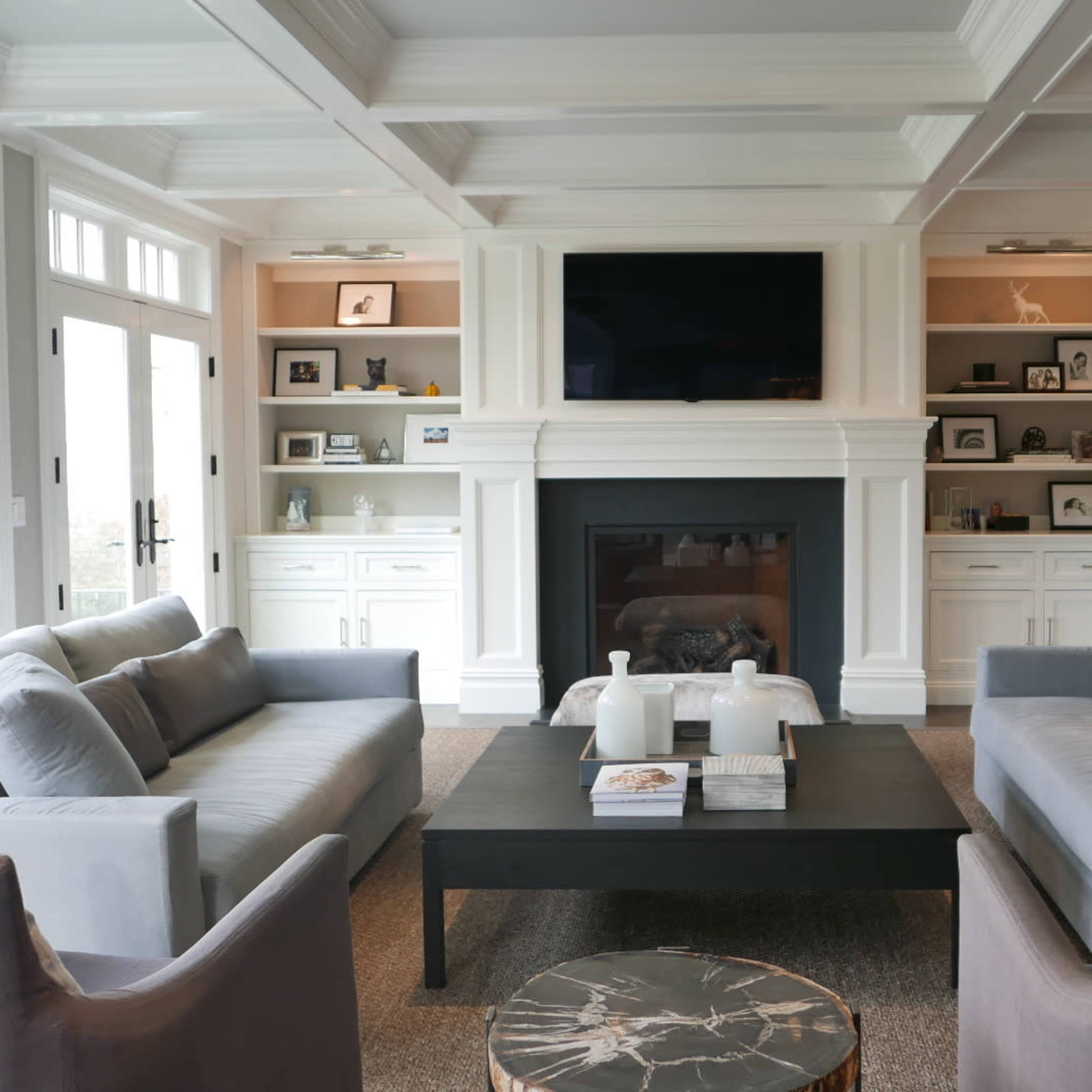 A modern living room with two gray sofas facing a coffee table, a fireplace, and built-in shelves displaying various items.