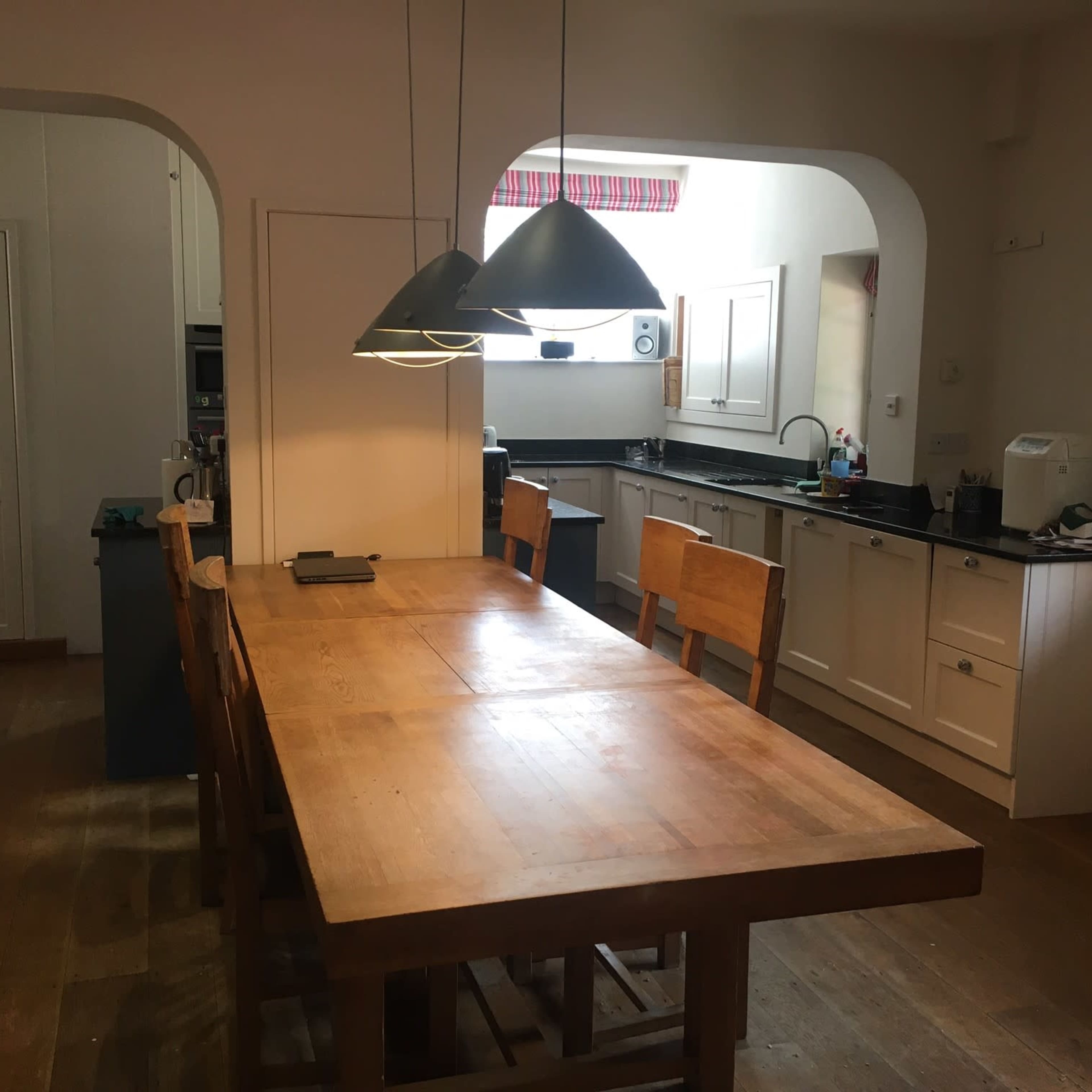 A modern kitchen with white cabinets, a large wooden dining table, and pendant lights hanging above it.