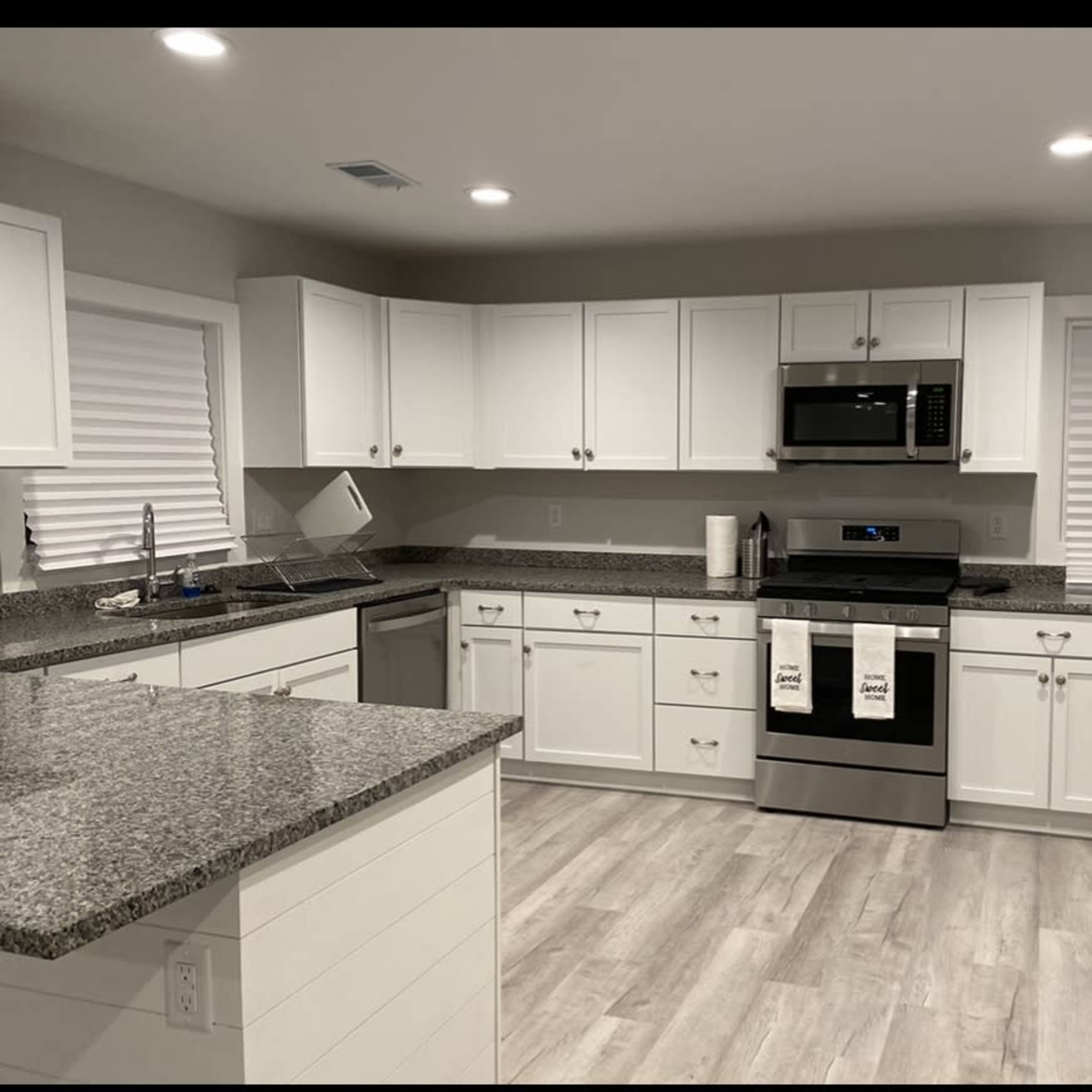 A modern kitchen features white cabinetry, stainless steel appliances, and a granite countertop with a light wood floor.