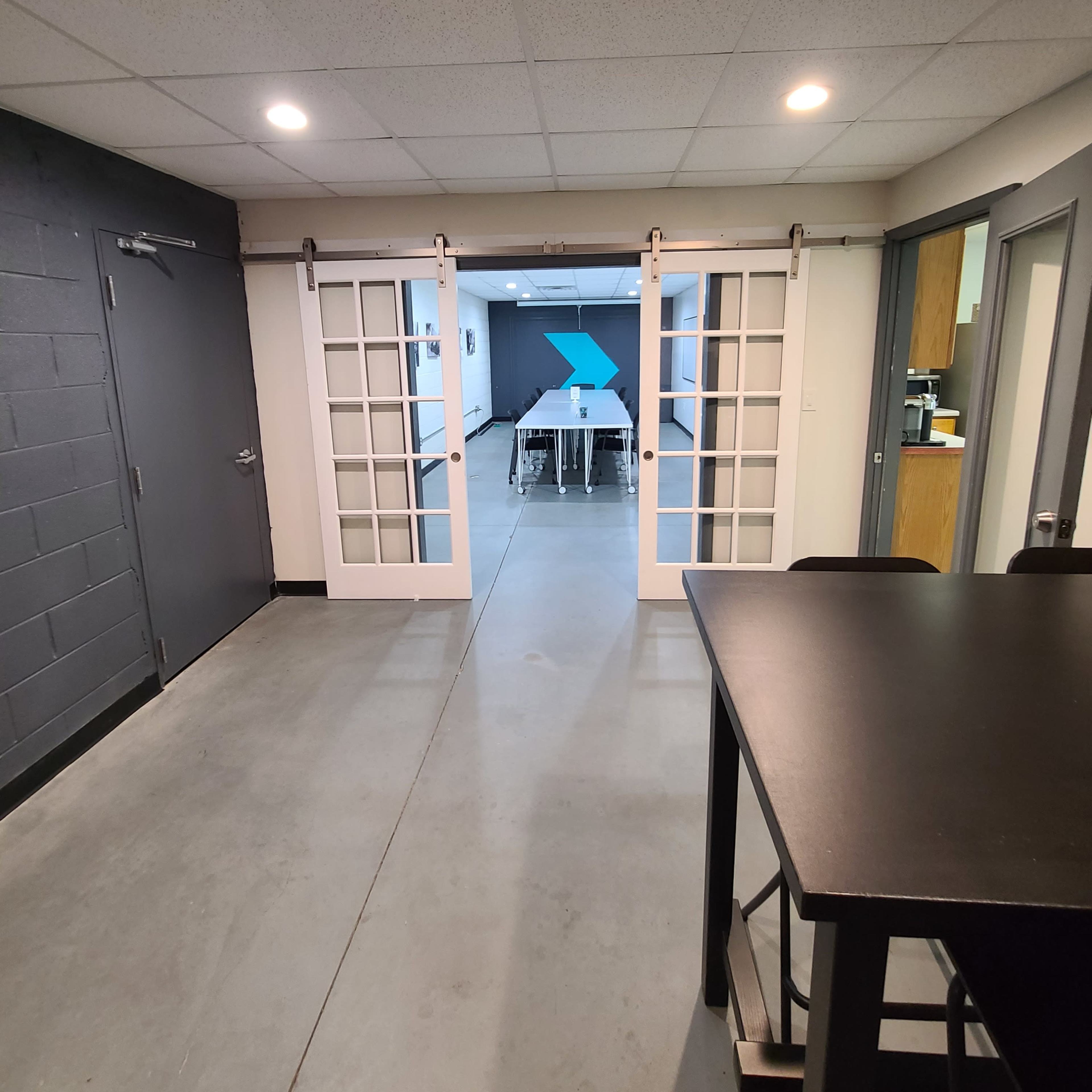 A hallway leading to a room with a table, framed by a set of sliding glass doors and a dark wall on the left.