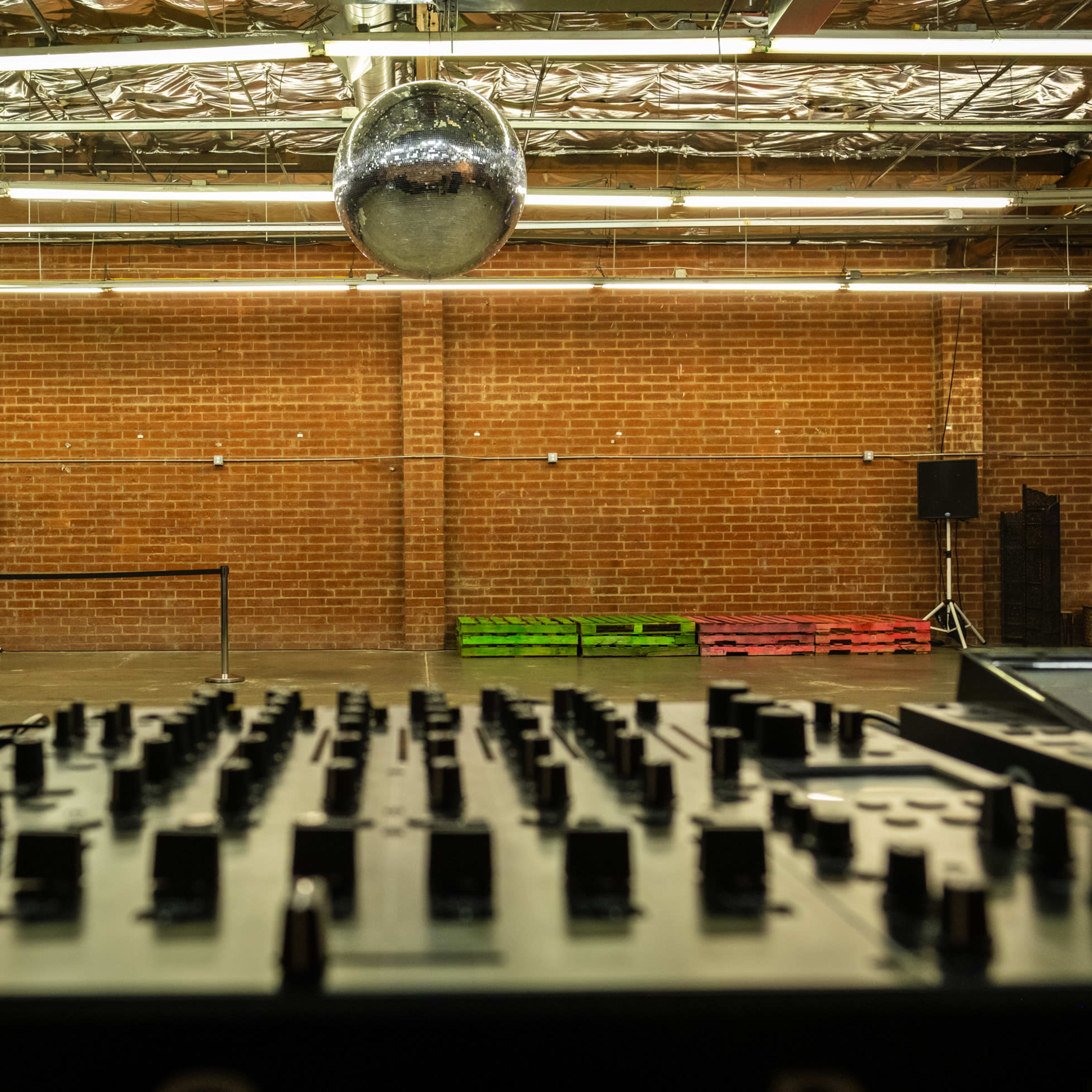 A DJ mixer is positioned in the foreground with a disco ball hanging above an empty warehouse space with brick walls.
