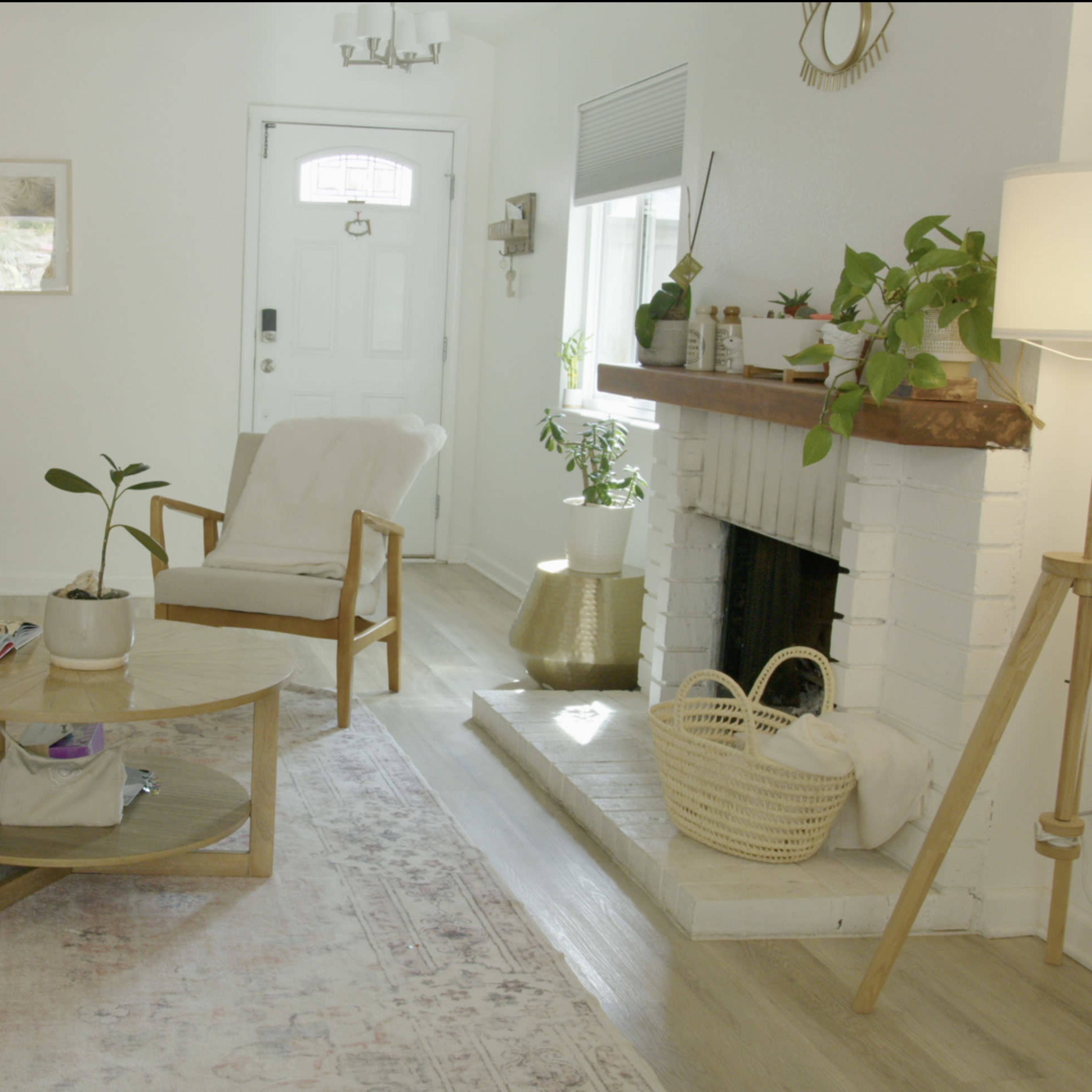 A bright living room features a cozy seating area with a round coffee table, a fireplace with plants, and a decorative mirror on the wall.