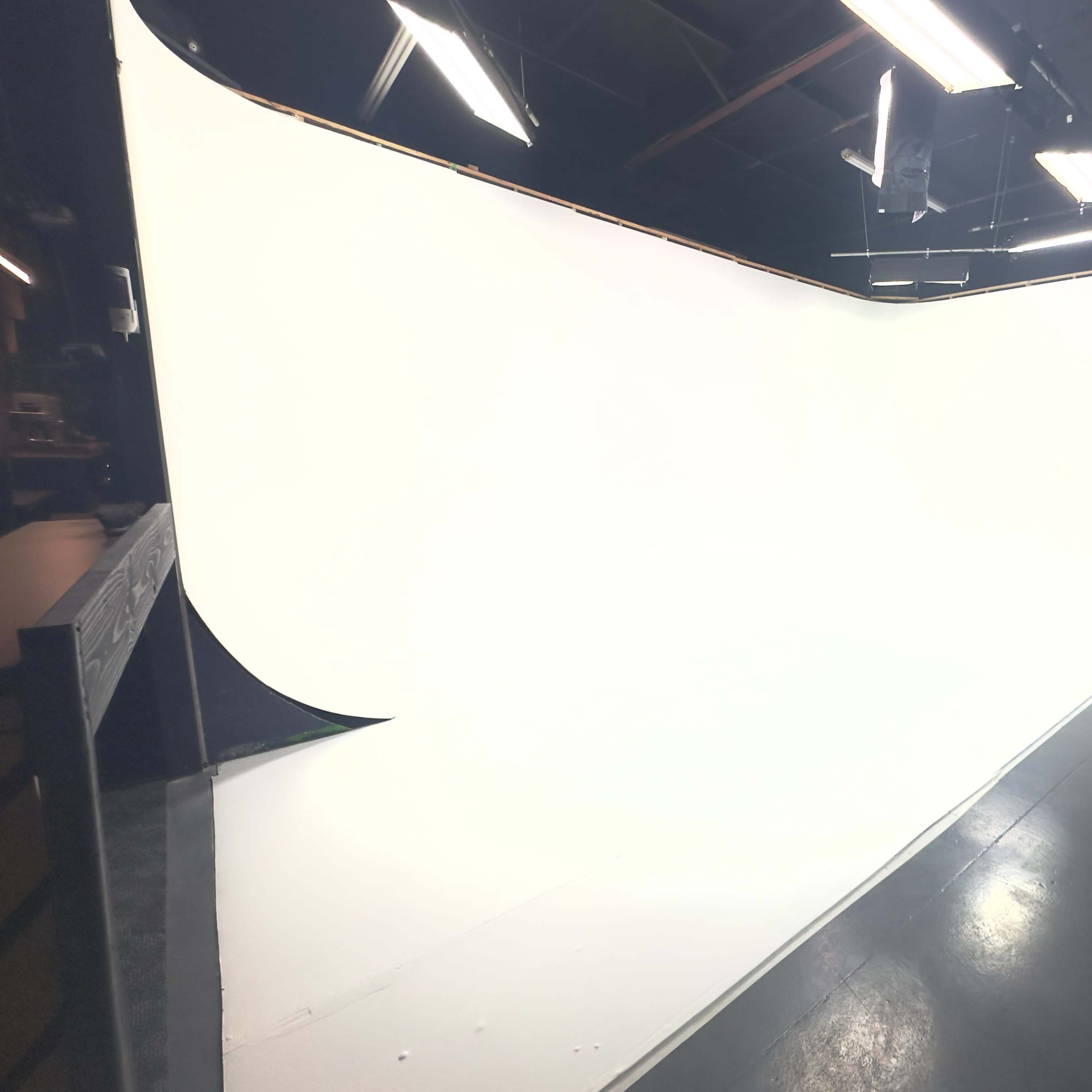 A large, curved white backdrop in a studio space with overhead lights and equipment visible.