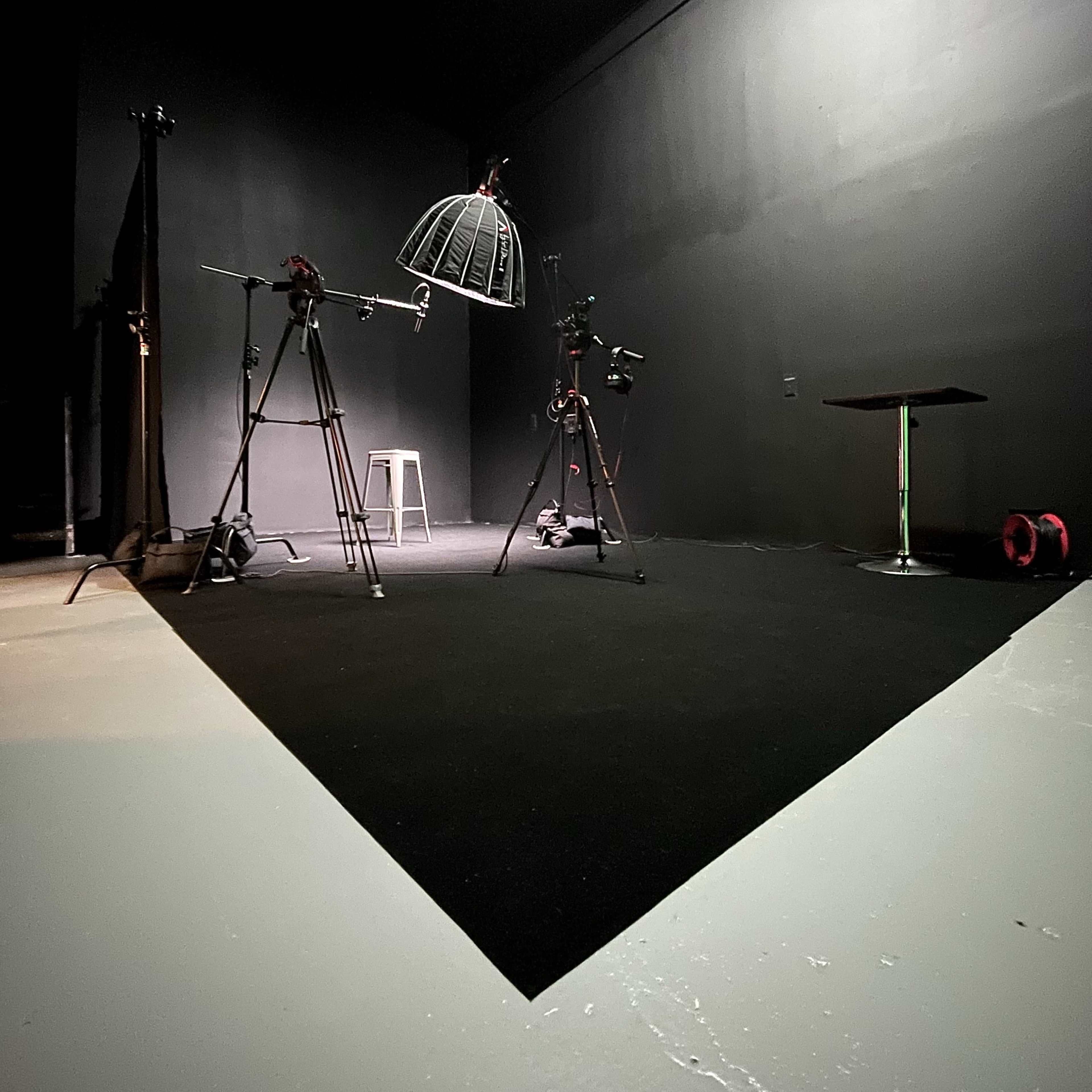 A dark studio space with two camera tripods, a light fixture, and a small table on a black floor.