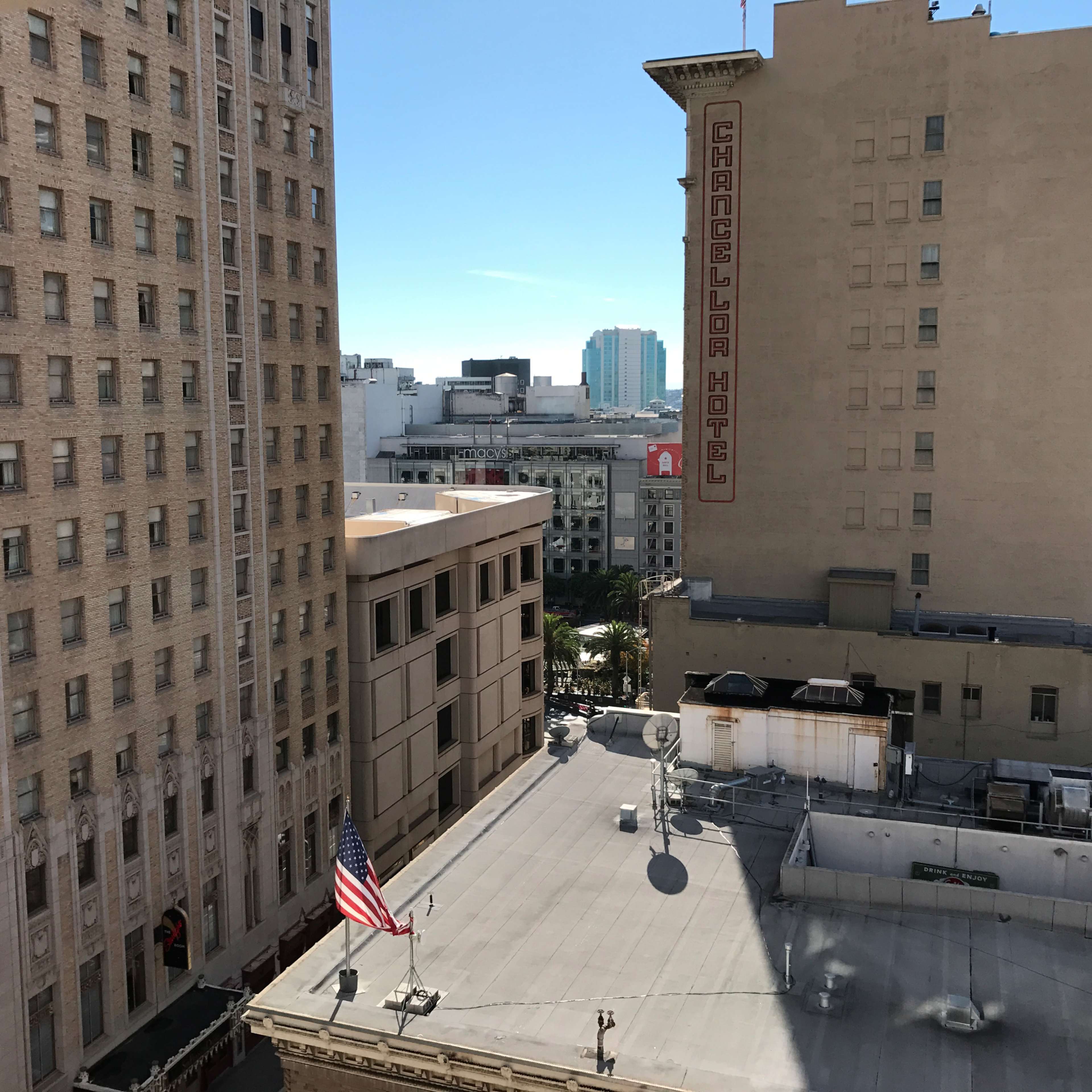 A view of buildings in an urban area, featuring an American flag and the sign for the Chancelor Hotel on a sunny day.