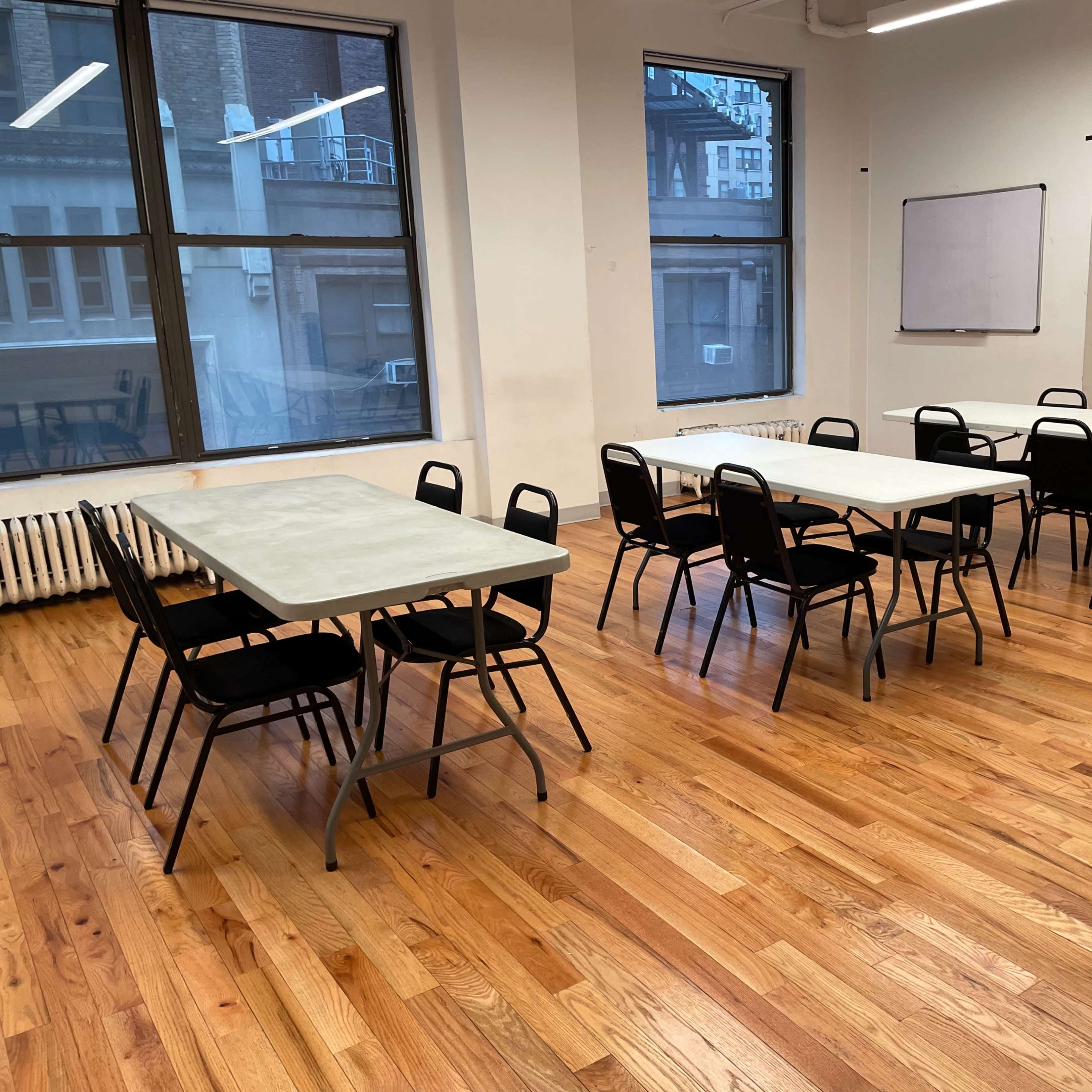 A spacious room with hardwood floors contains several tables and chairs arranged neatly.