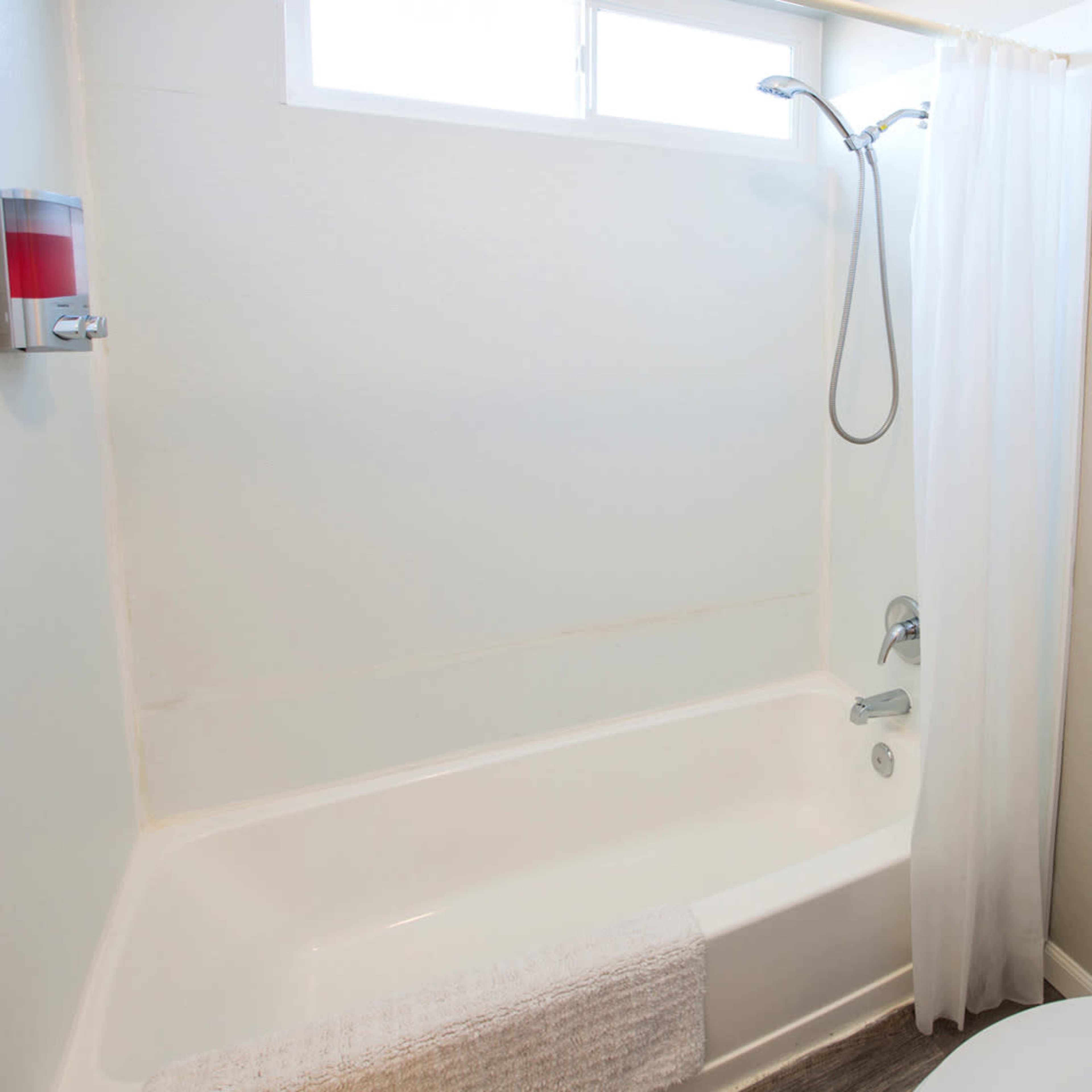A small bathroom featuring a bathtub with a showerhead, a white shower curtain, and a toilet next to it.