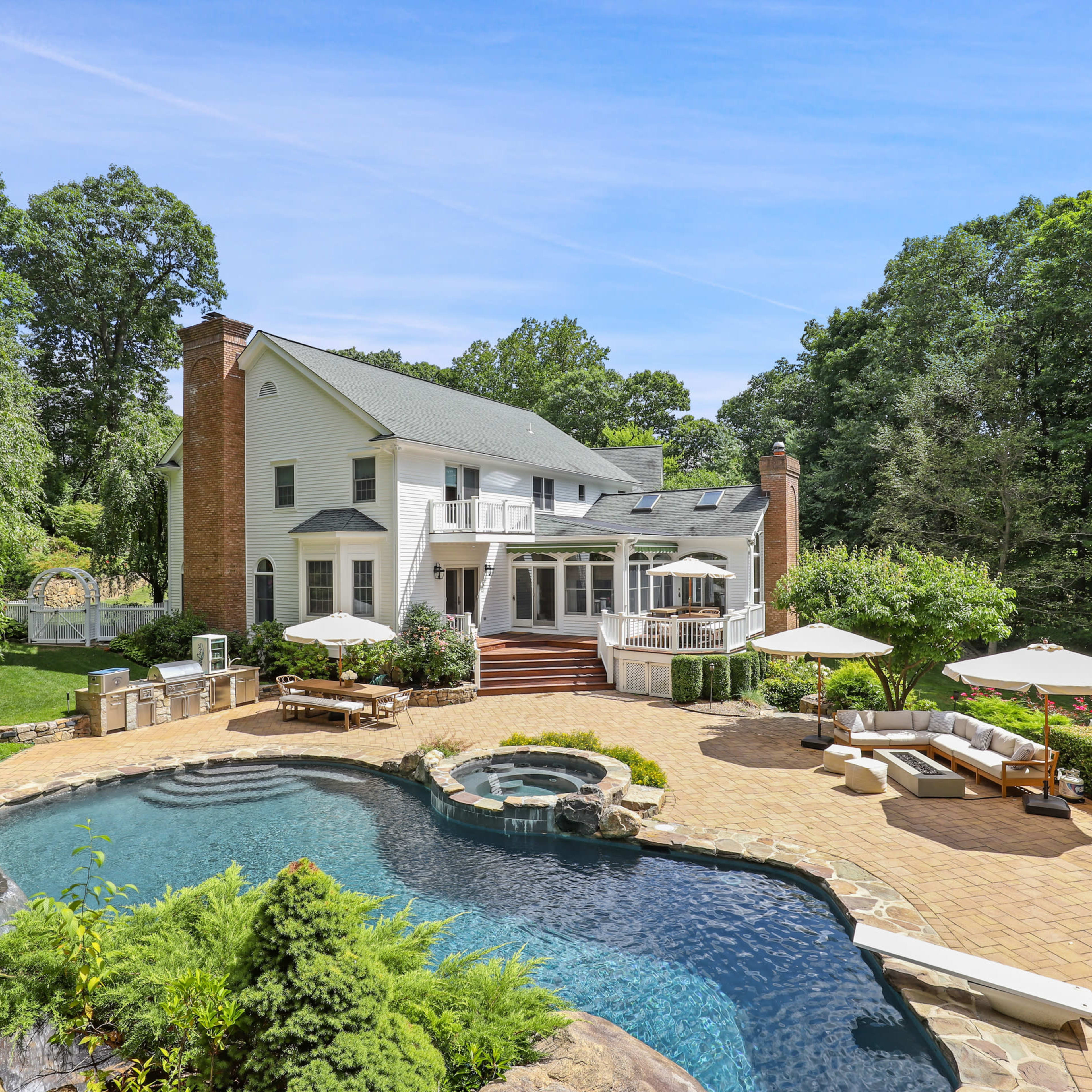 A large house with a pool and patio is surrounded by trees and landscaped gardens.