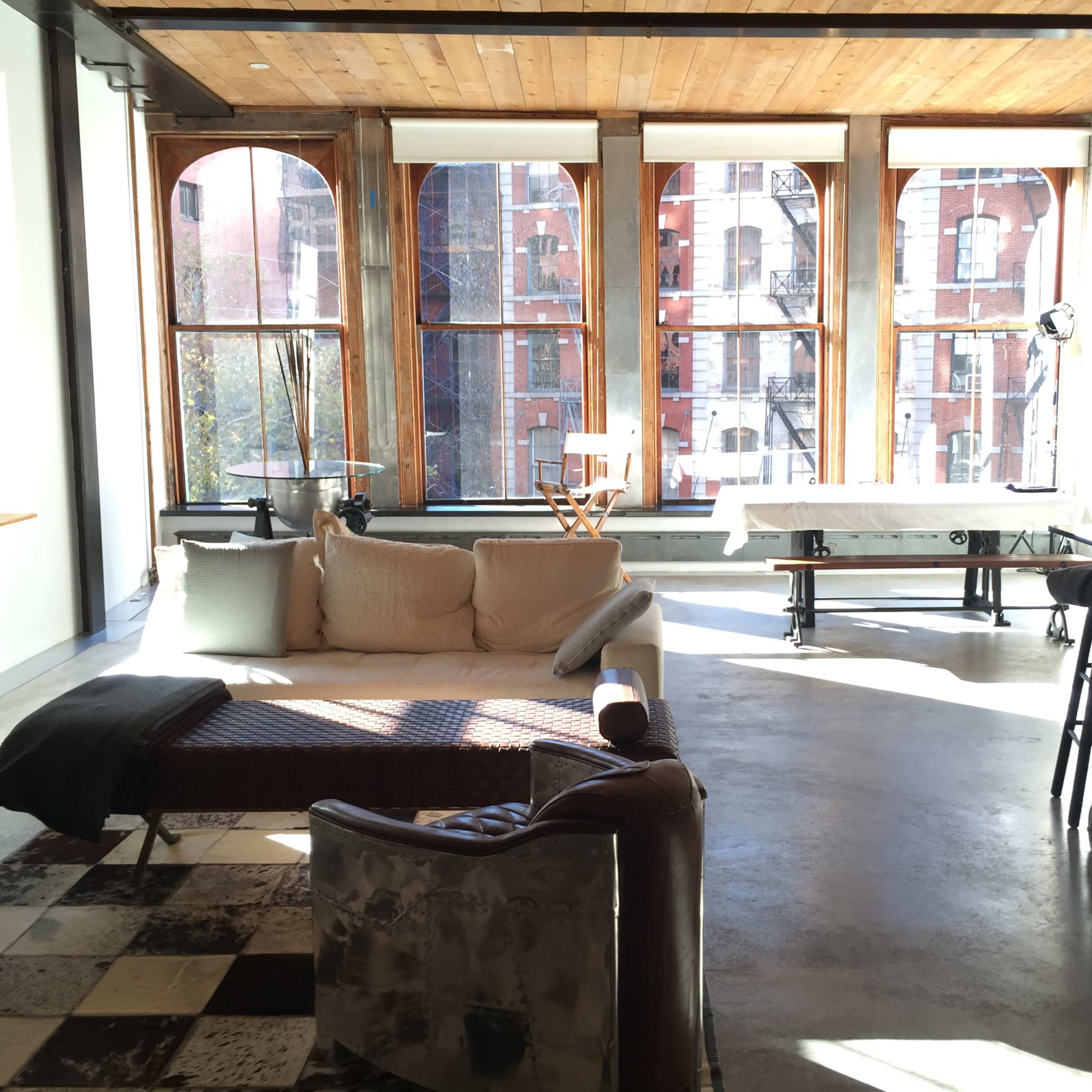 A bright, open living space with large windows, a sectional sofa, a patterned rug, and a glass-topped table.