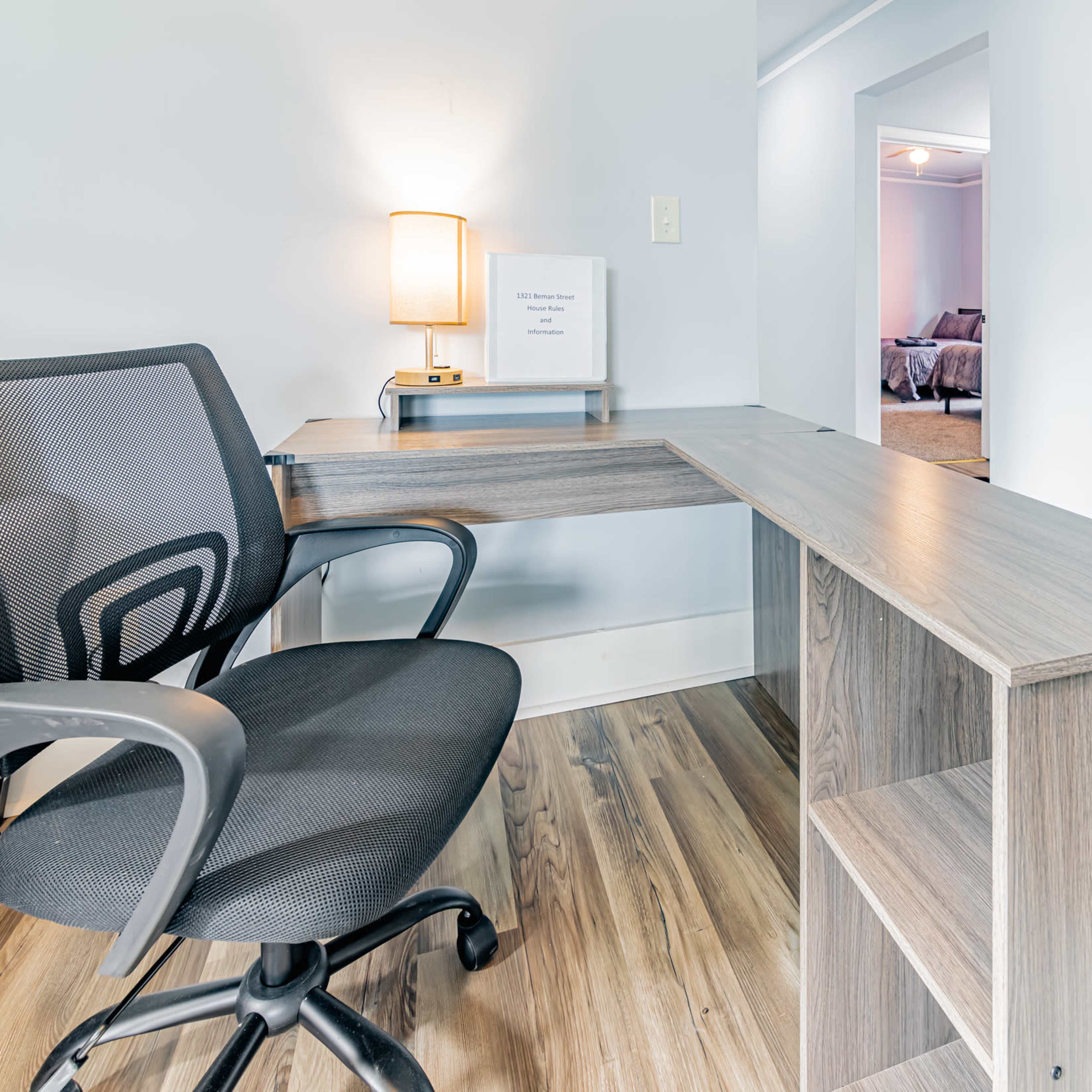 A modern office desk with a black mesh chair, positioned in a well-lit room with a doorway leading to another space.