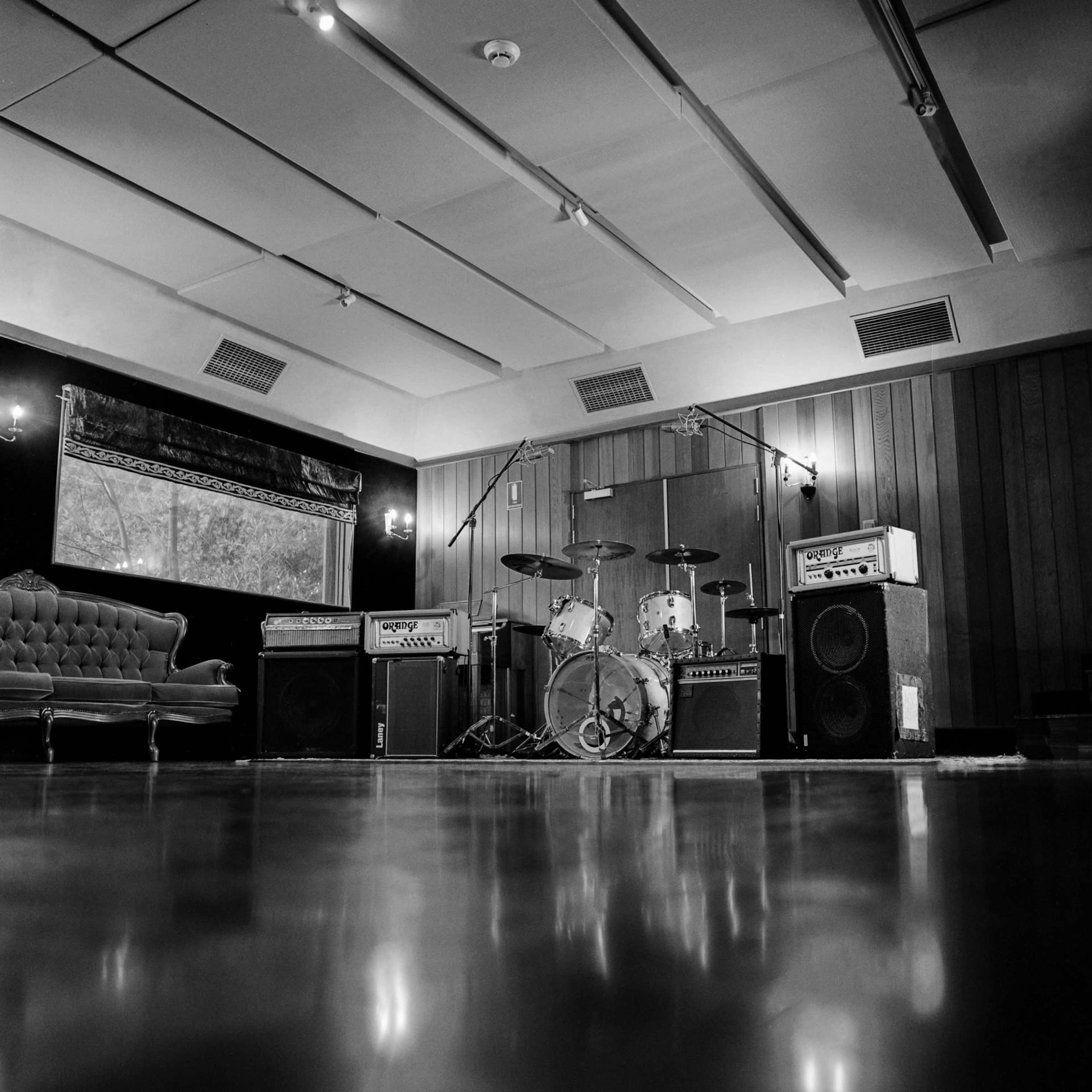 A music studio with a drum set, amplifiers, and a vintage couch in a spacious, polished room.