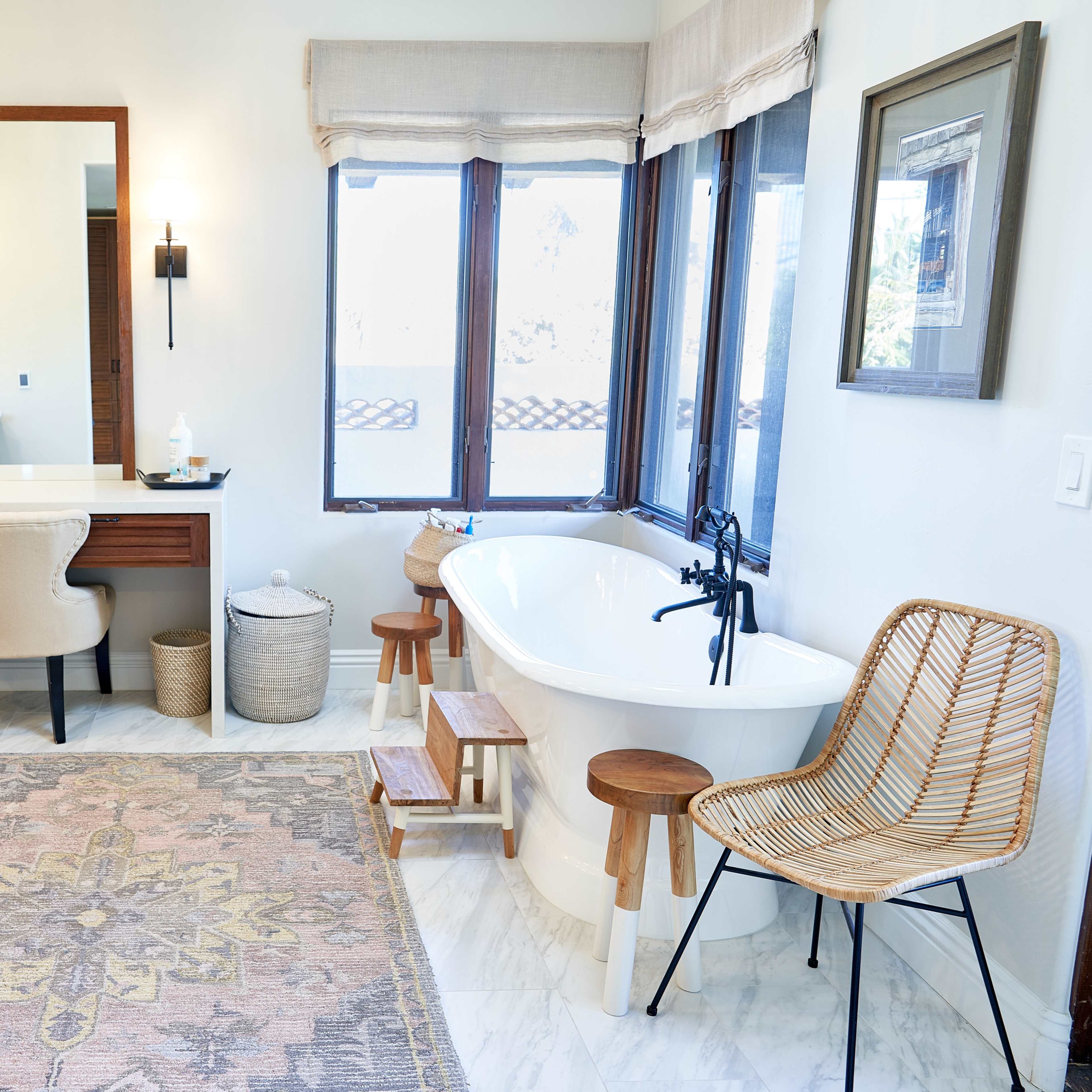 A spacious bathroom featuring a freestanding bathtub, a large mirror above a vanity, and natural light coming through multiple windows.