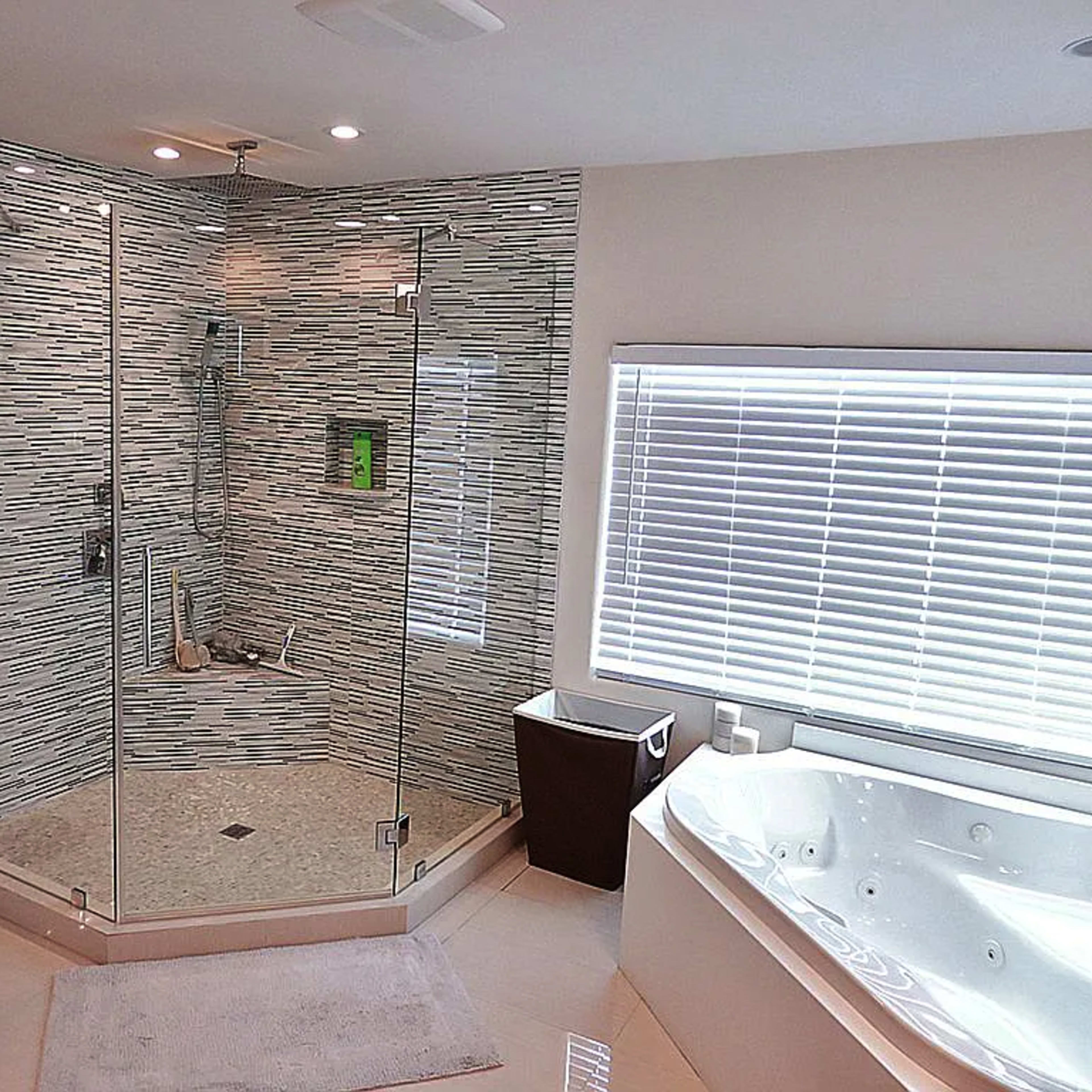 A modern bathroom featuring a glass shower enclosure with tiled walls and a separate jacuzzi tub beside a window with blinds.