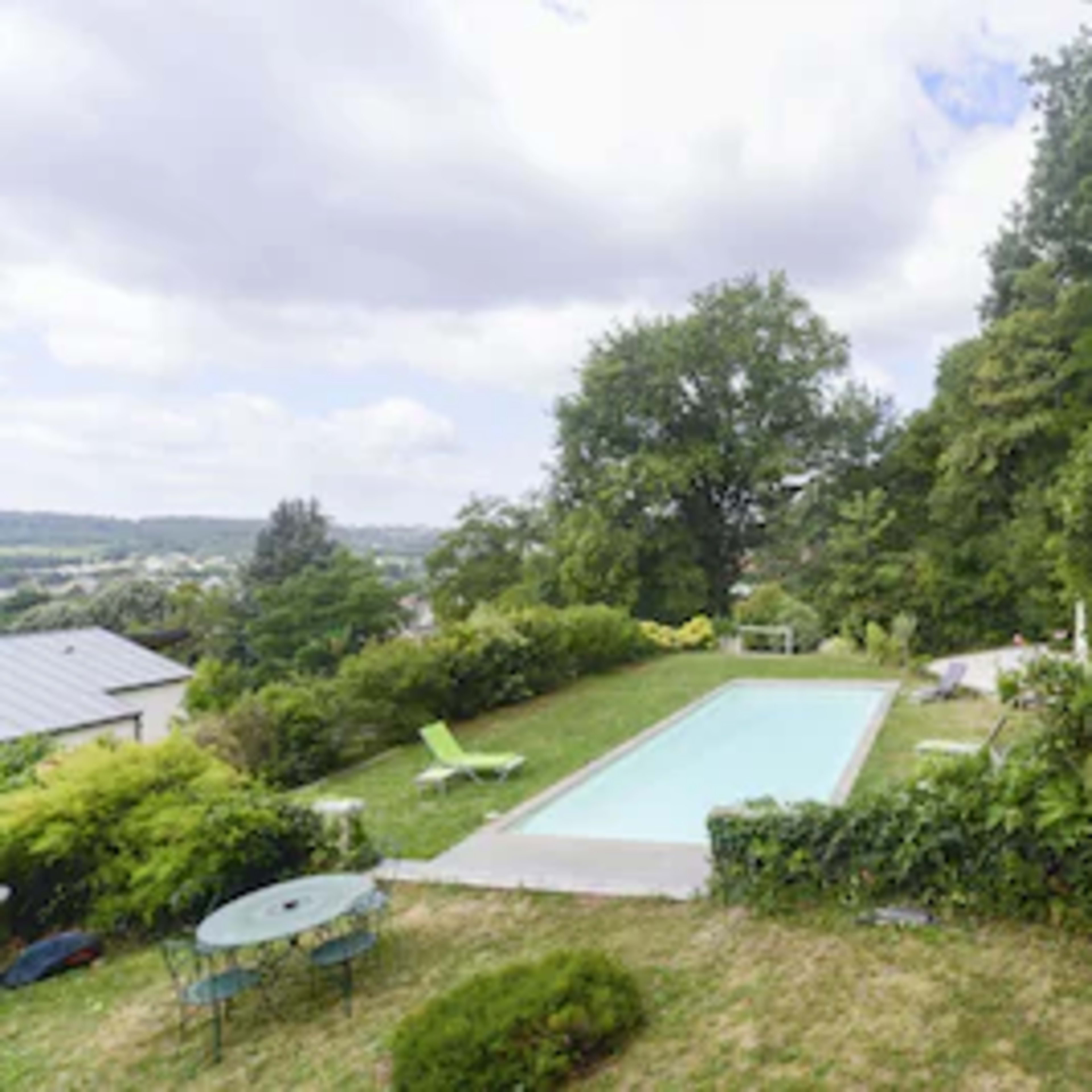 A swimming pool is surrounded by greenery and outdoor seating in a landscaped garden.
