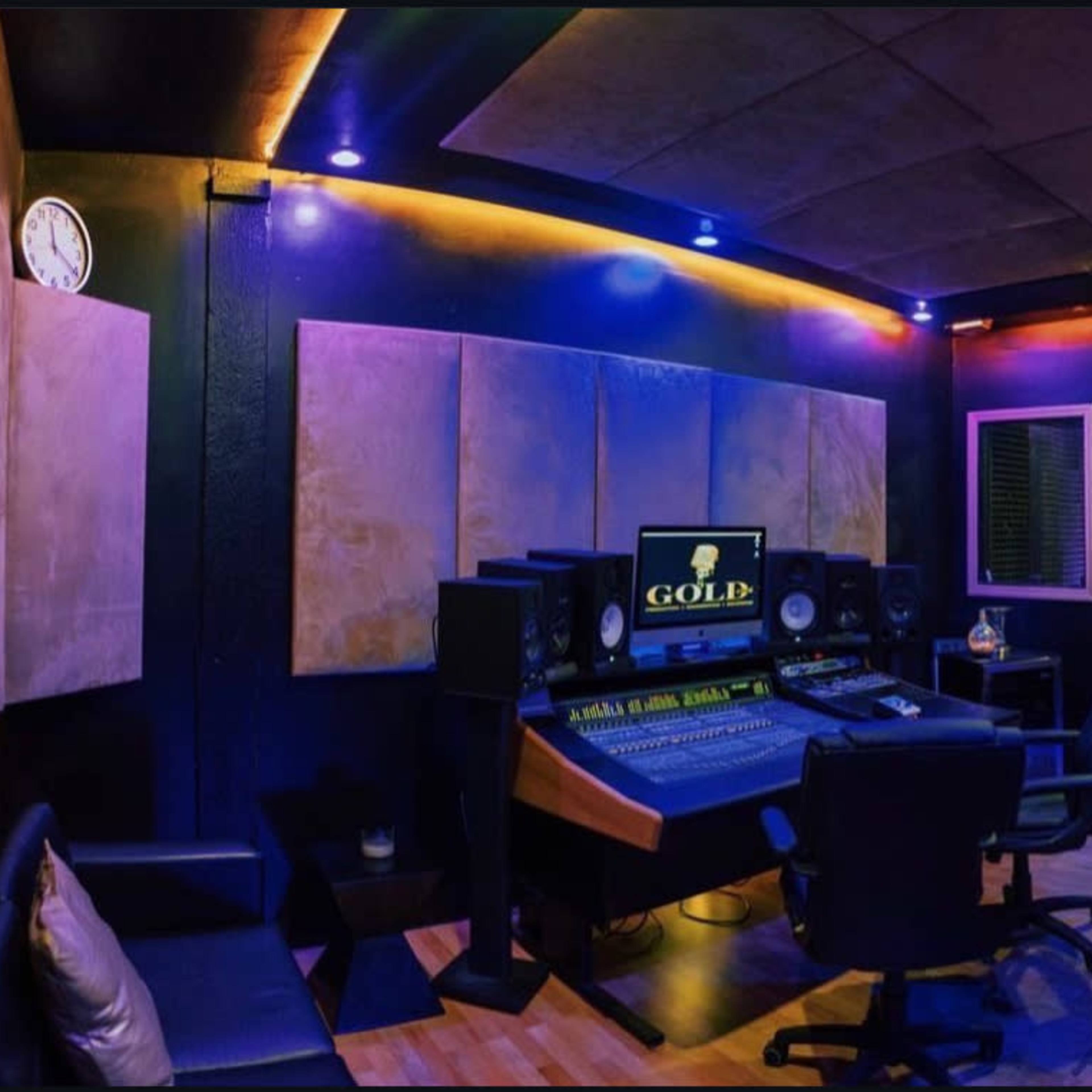 A modern music recording studio with a central mixing desk, speakers, and soundproof panels on the walls.