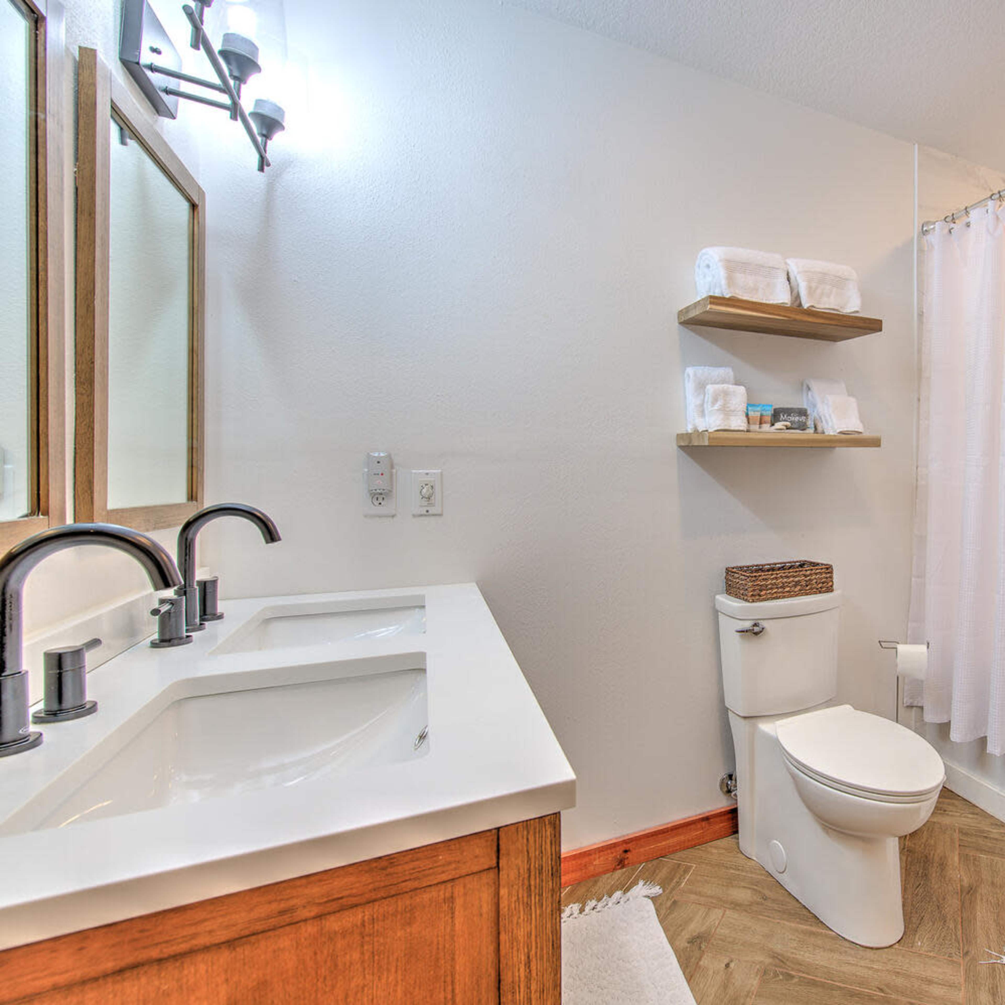 A clean bathroom featuring a double sink vanity, a bathtub with a shower curtain, and wooden shelves with folded towels.
